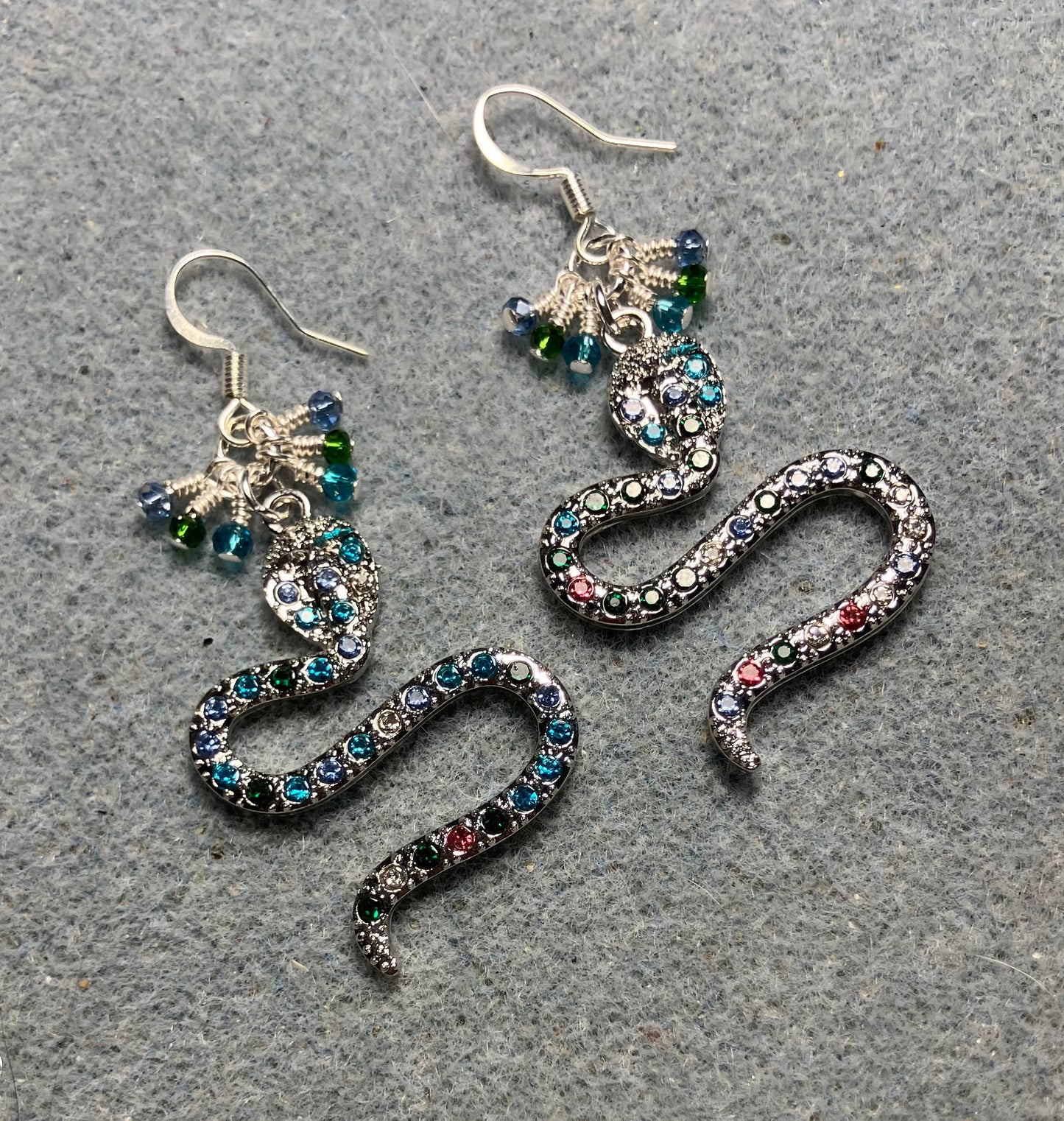 Silver and colored rhinestone coiled snake charm earrings adorned with tiny dangling turquoise, dark green, and light blue Chinese crystal beads.