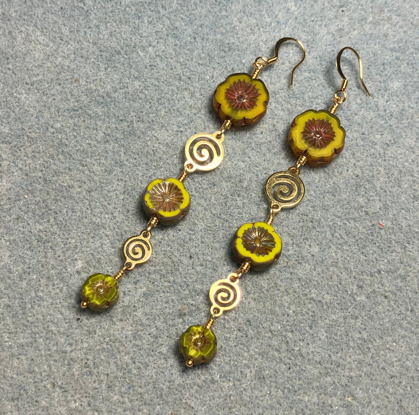 Extra long mustard green flower bead earrings made with three sizes of mustard green Czech glass pansy beads joined by gold swirly connectors.