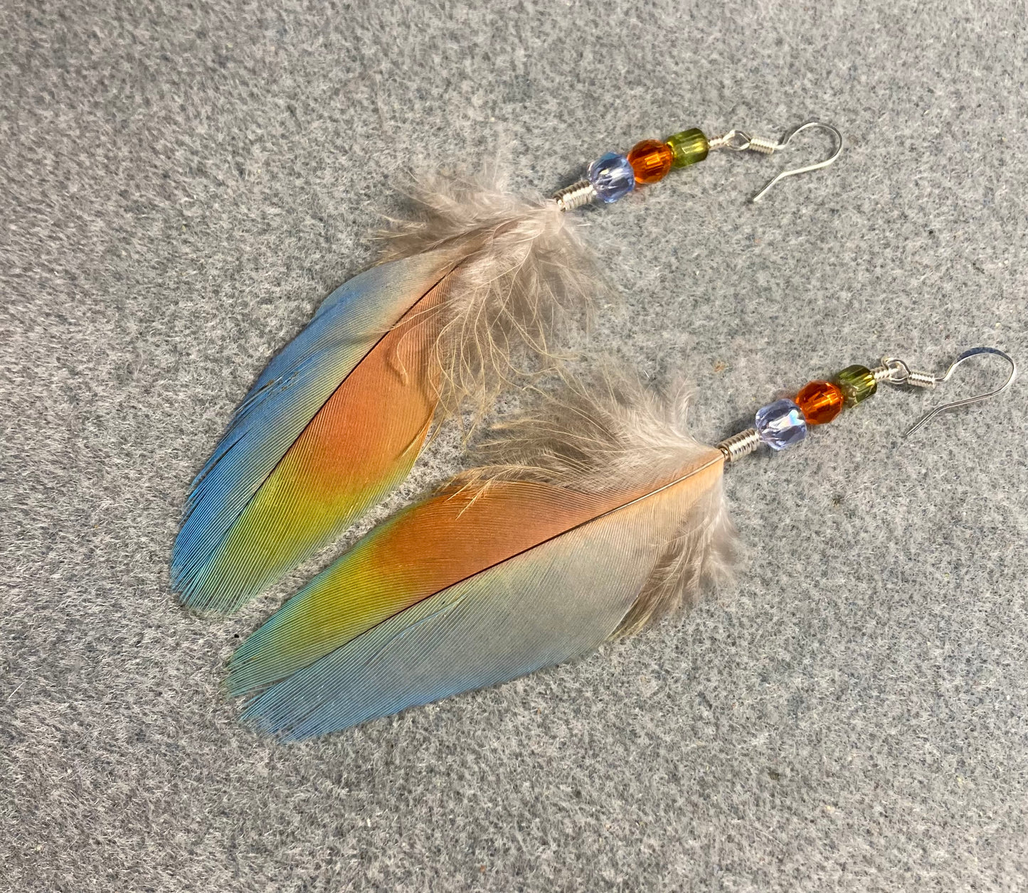 Light blue and orange scarlet macaw feather earrings adorned with light blue, orange, and green Czech glass beads.