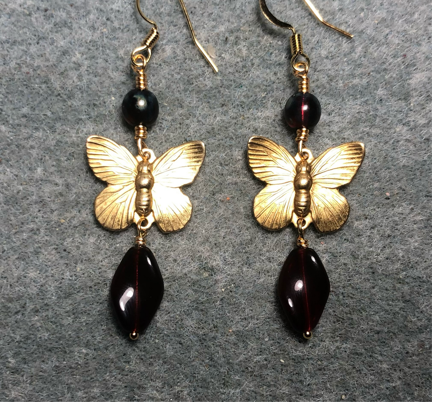 Gold butterfly charm connector earrings adorned with dark red Czech glass twist beads and dark red Czech glass beads.