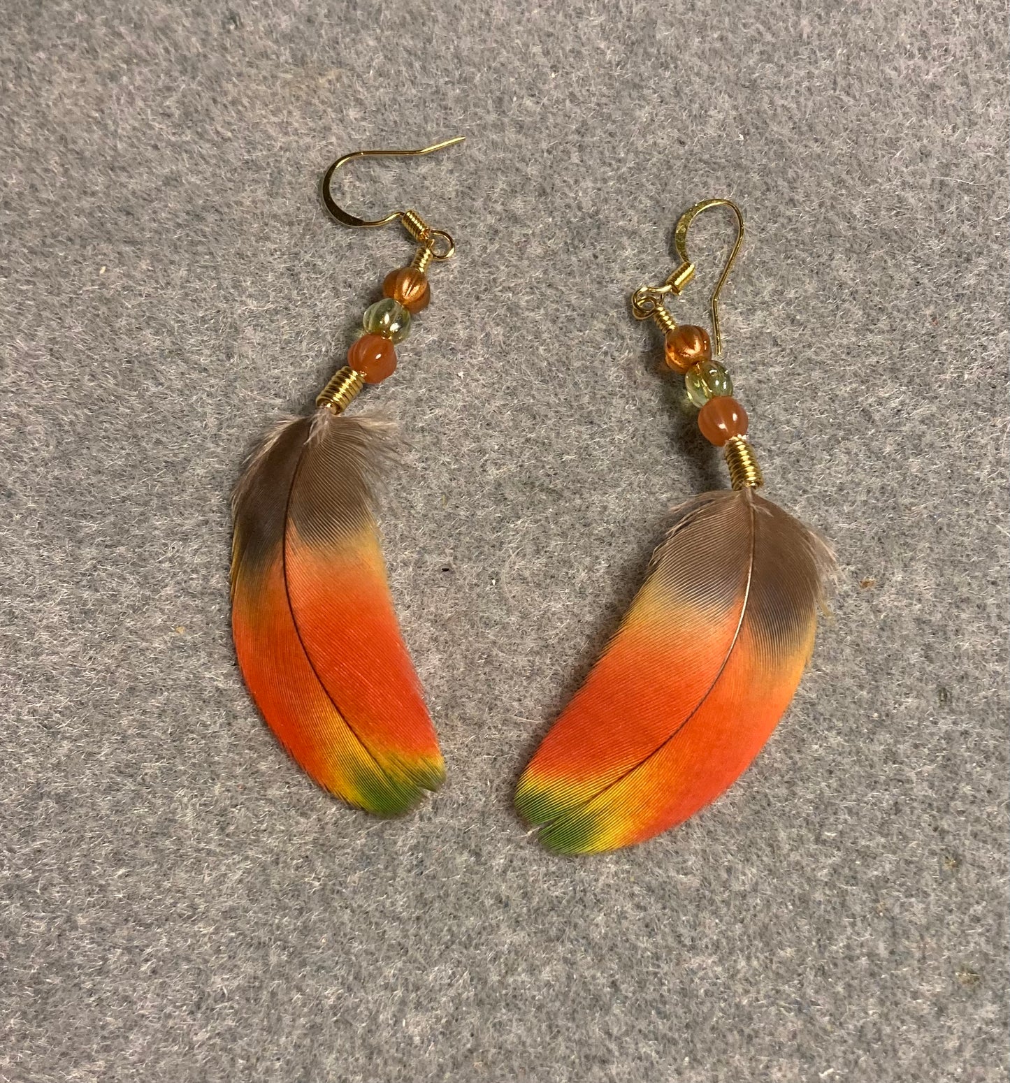 Orange, yellow, and green scarlet macaw feather earrings adorned with small orange and green Czech glass melon beads.