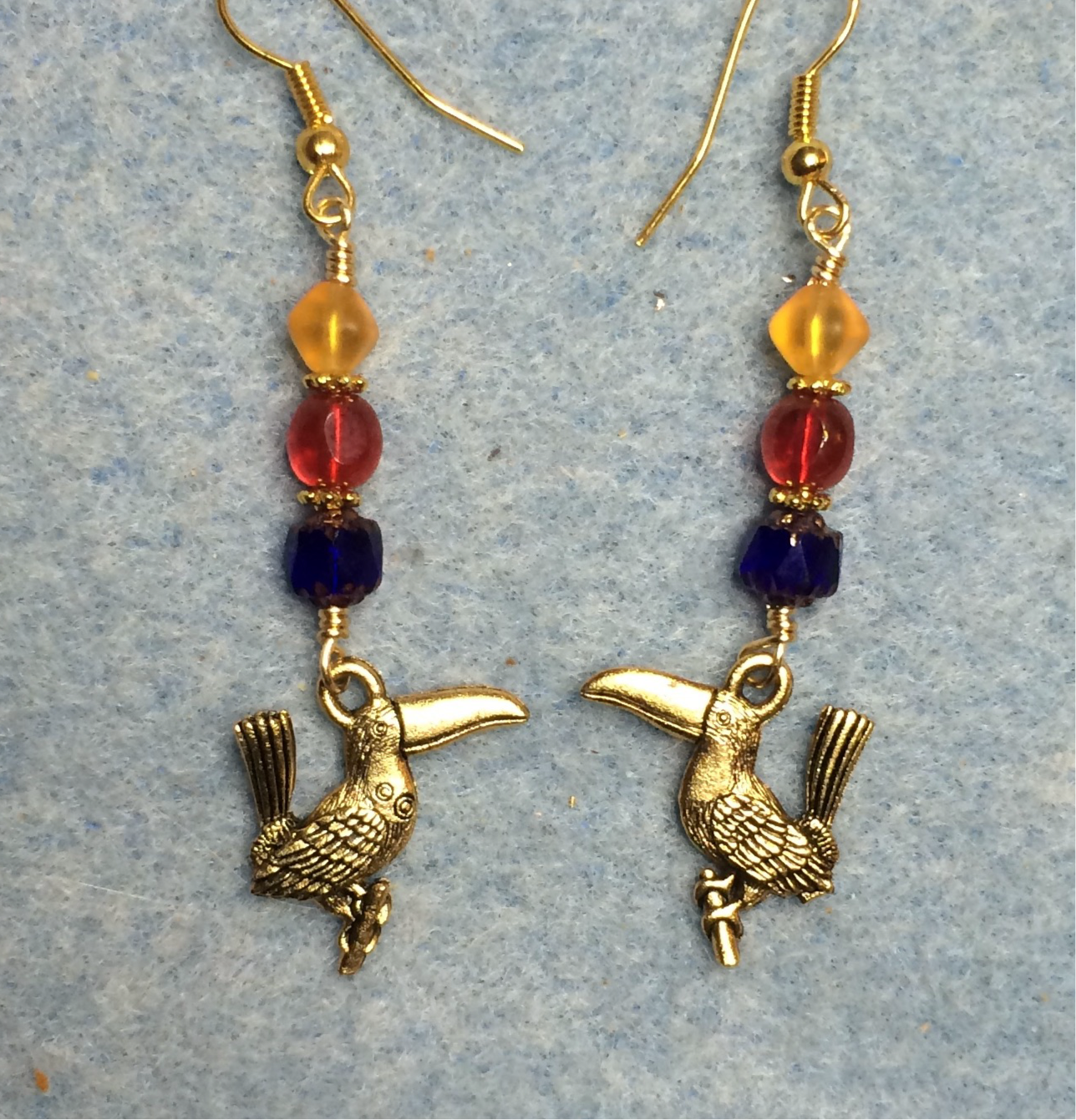 Gold toucan charm earrings adorned with blue, red, and yellow Czech glass beads