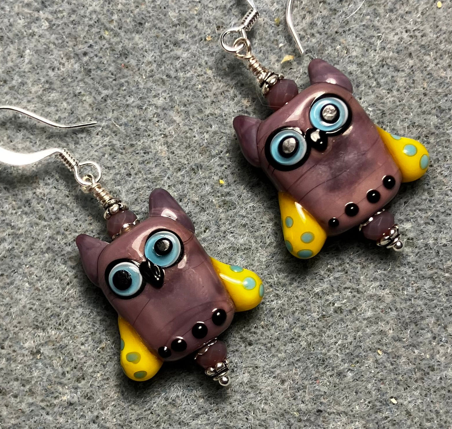 Violet, yellow, and blue lamp work owl bead earrings adorned with violet Chinese crystal beads.