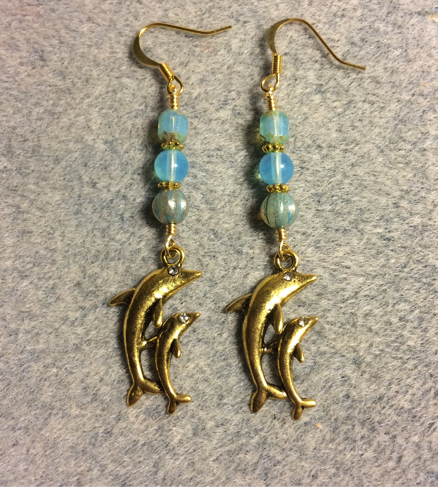 Gold pair of dolphin charm earrings adorned with milky turquoise Czech glass beads