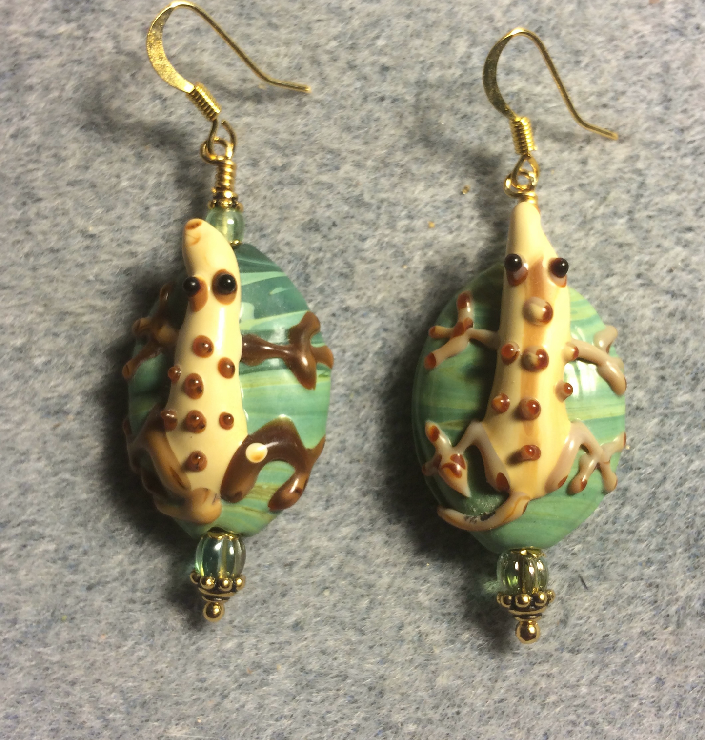 Large beige and green lamp work lizard bead earrings adorned with light green Czech glass beads.