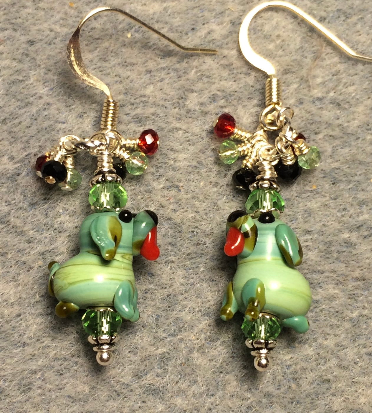 Tiny green lamp work puppy dog bead earrings adorned with green Chinese crystal beads and tiny dangling green, red, and black Chinese crystal beads.
