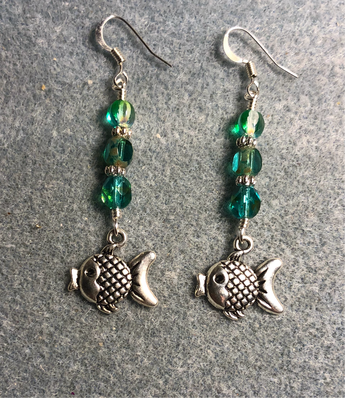 Silver fish charm earrings adorned with blue green Czech glass beads.