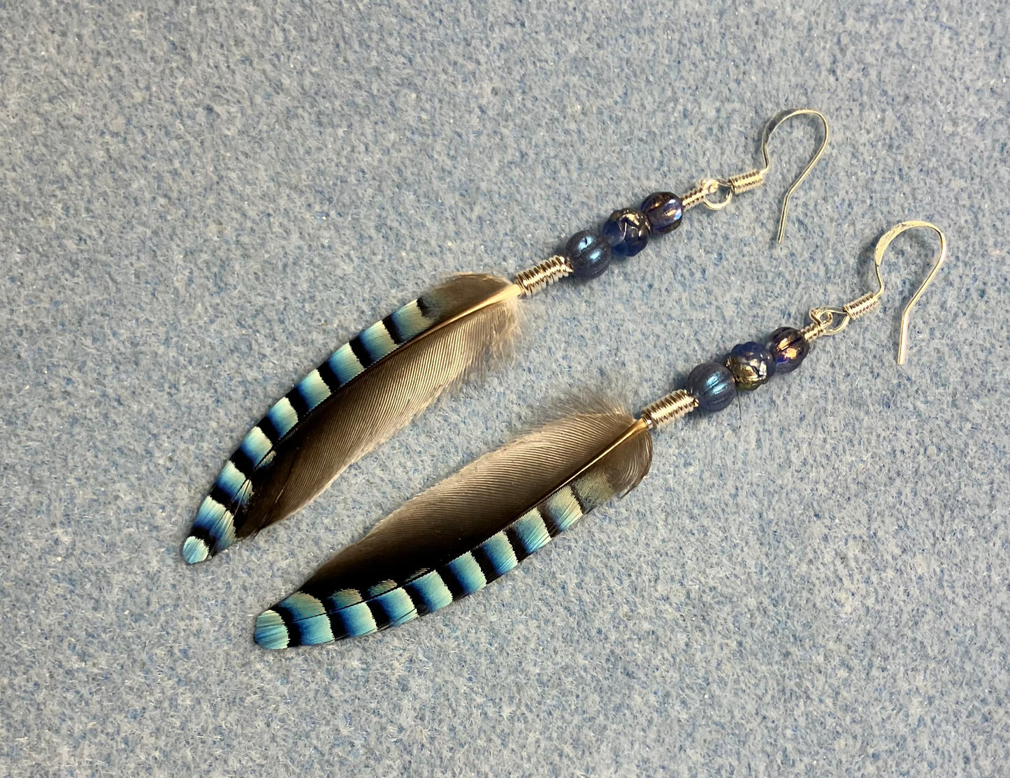 Small striped blue jay feather earrings adorned with small blue Czech glass beads.