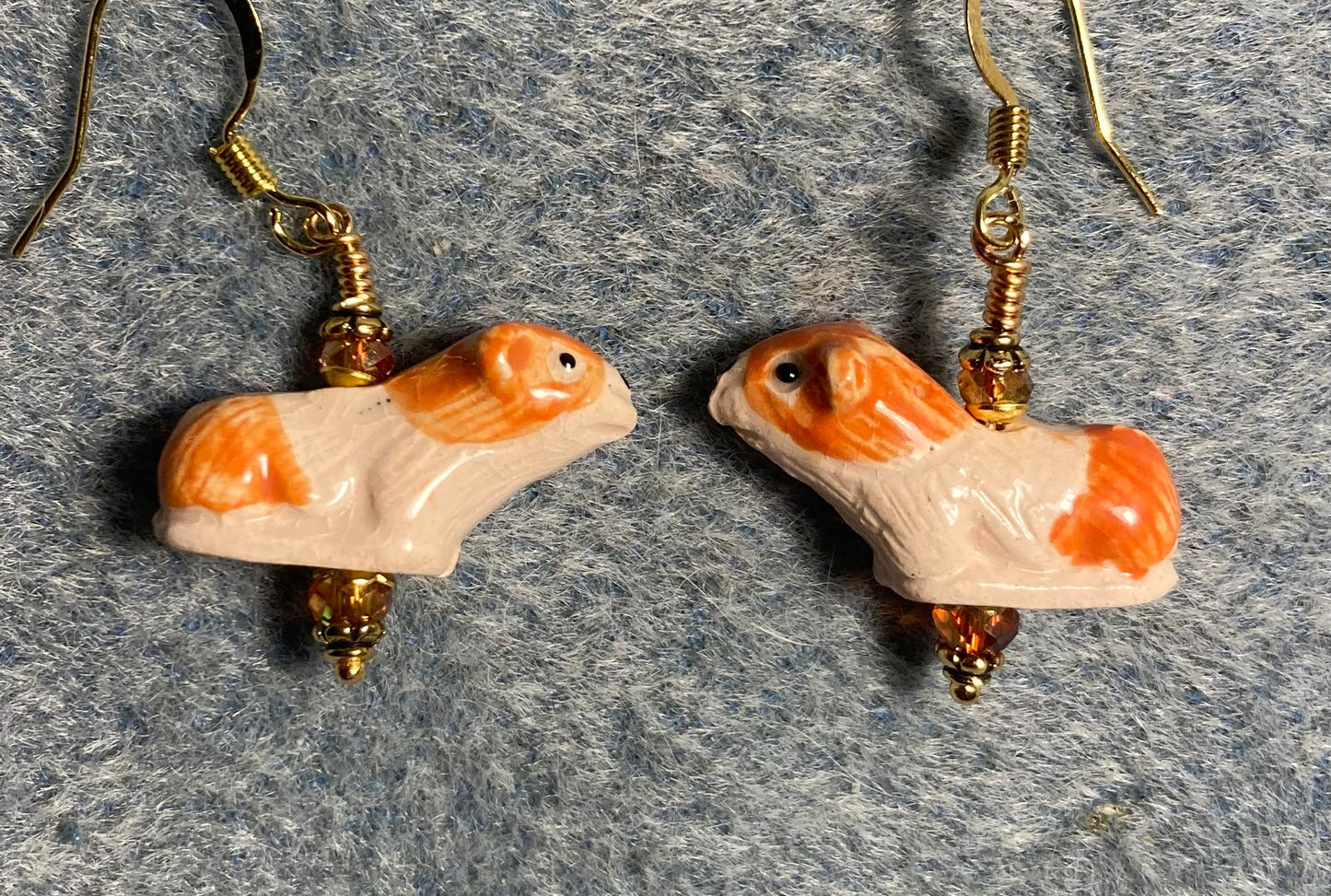 Small orange and white ceramic guinea pig bead earrings adorned with sparkly orange Chinese crystal beads.