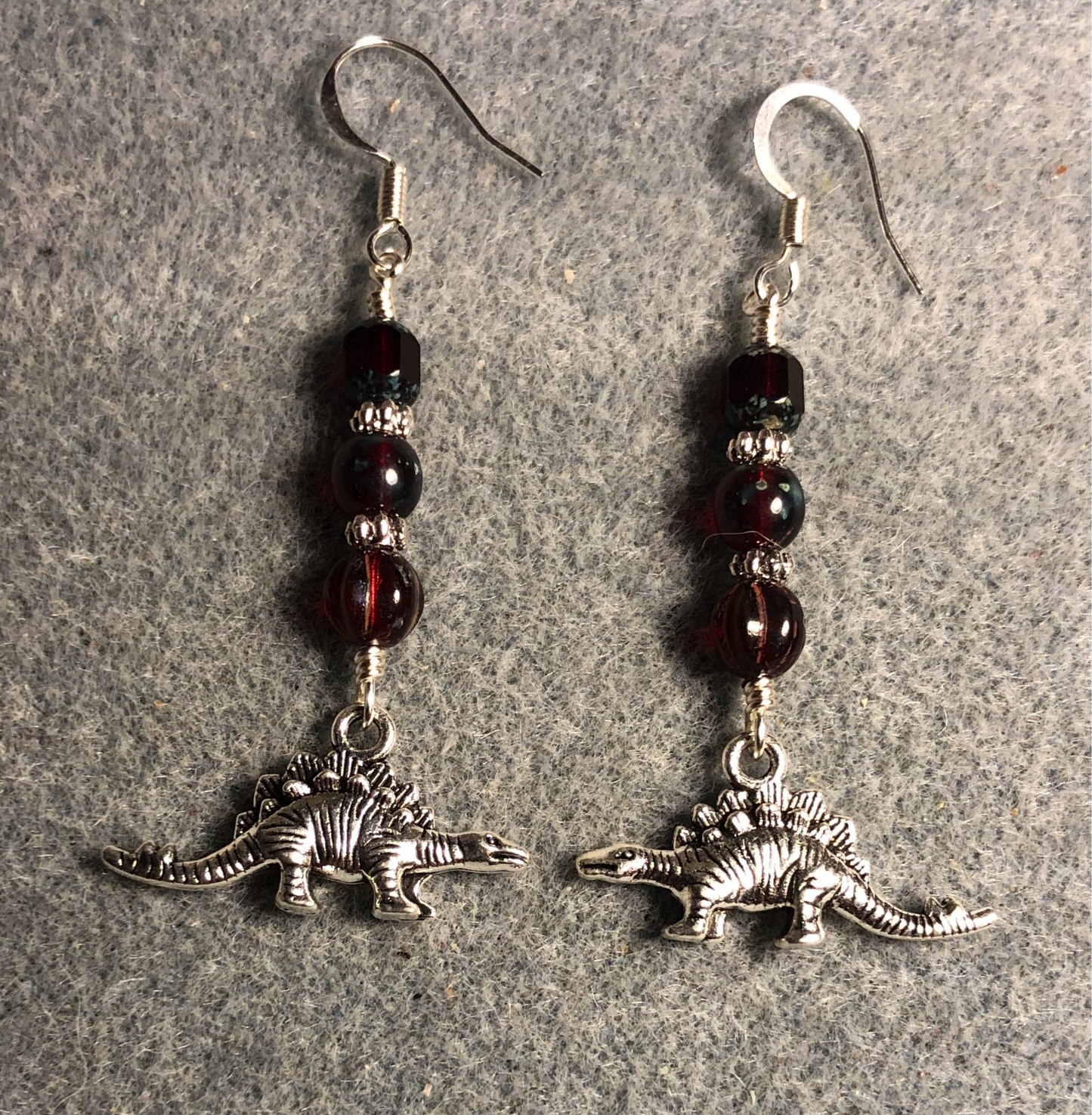 Silver stegosaurus charm earrings adorned with dark red Czech glass beads