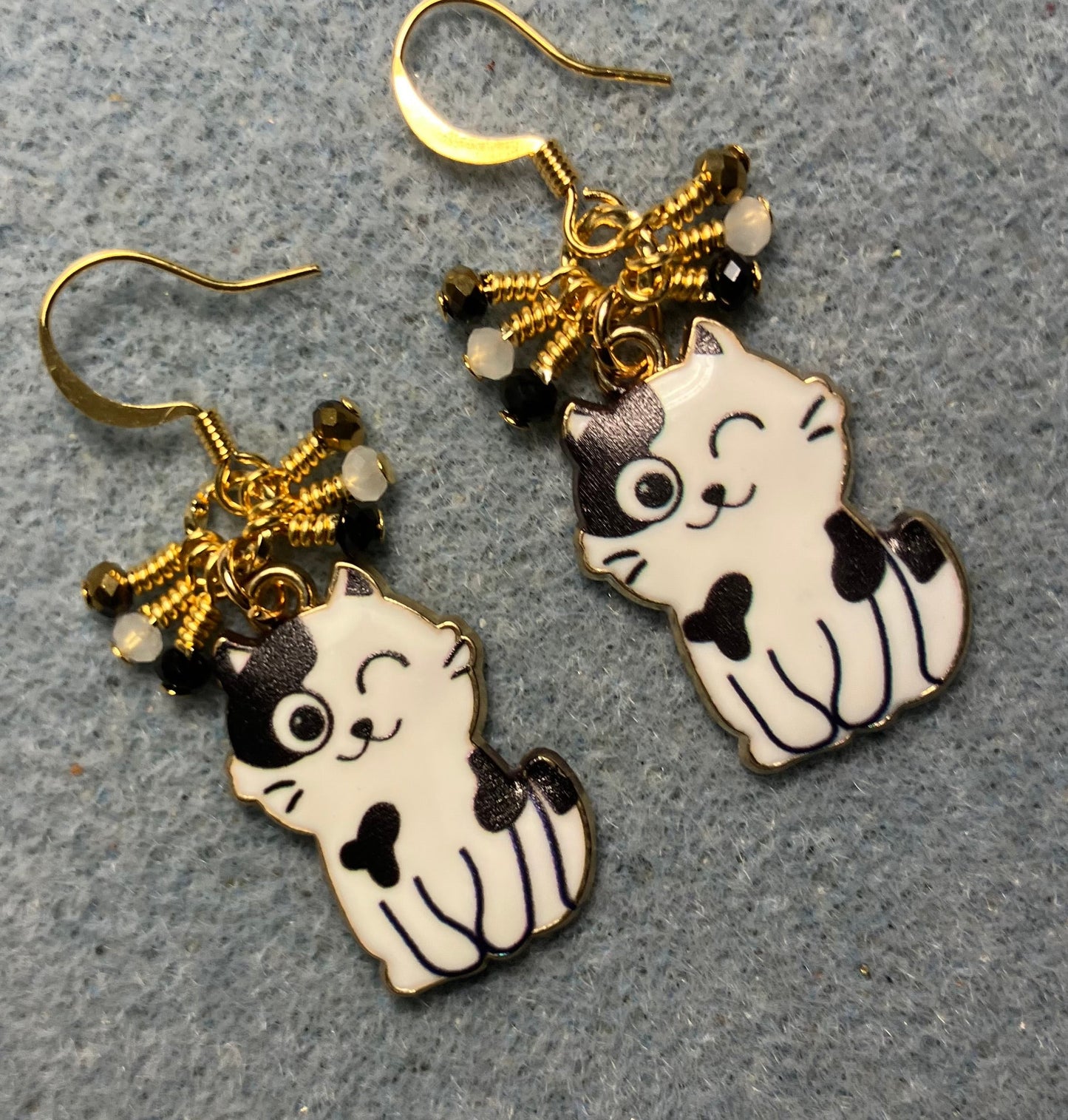Black and white enamel cat charm earrings adorned with tiny dangling black, white, and gold Chinese crystal beads.