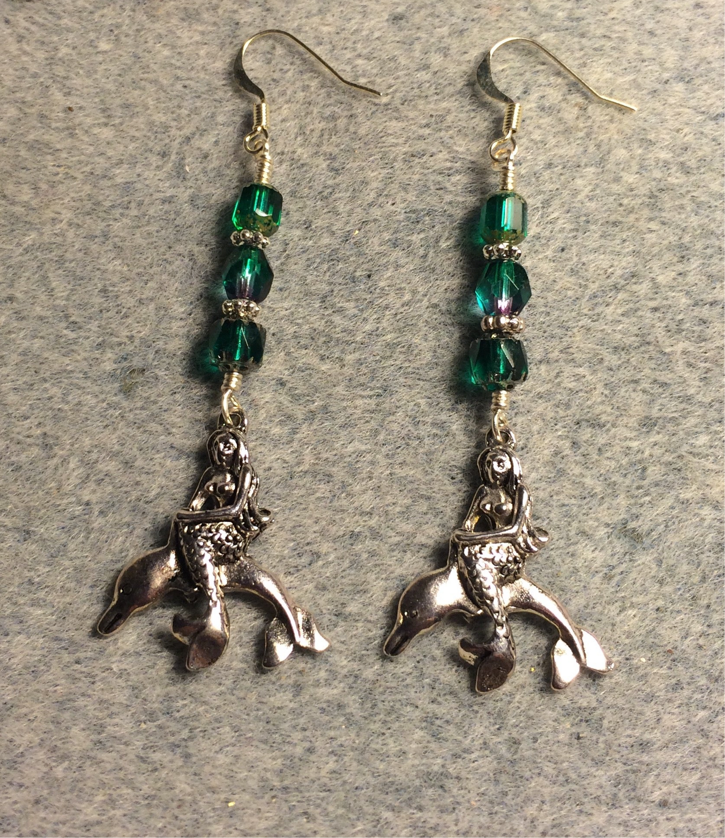 Silver mermaid sitting on a dolphin charm earrings adorned with teal Czech glass beads