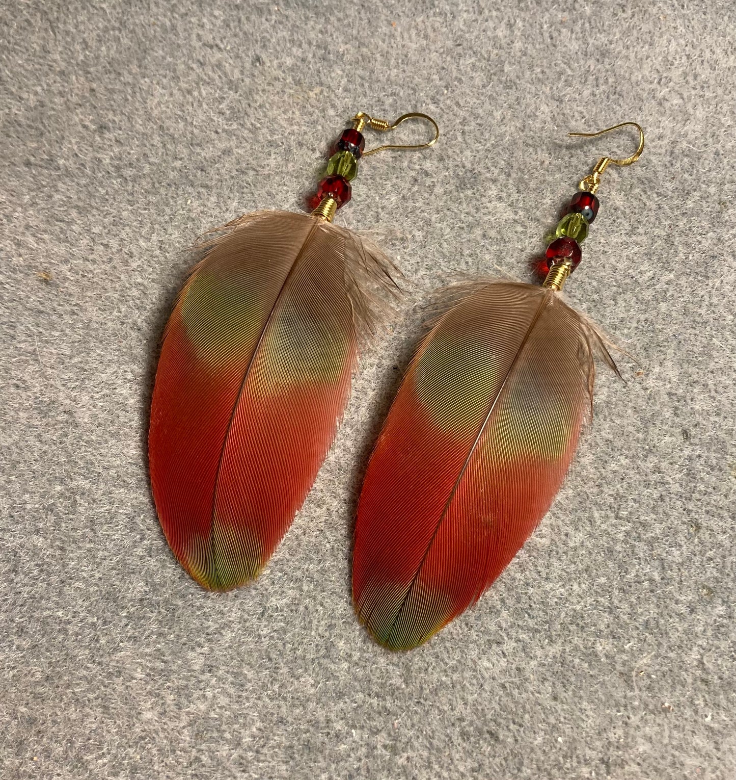 Dark red and green greenwinged macaw feather earrings adorned with red and green Czech glass beads.