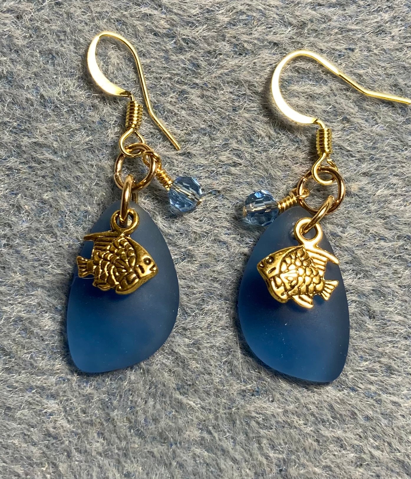 Small dark blue sea glass pendant bead earrings adorned with small gold angelfish charms and small dark blue Chinese crystal beads.