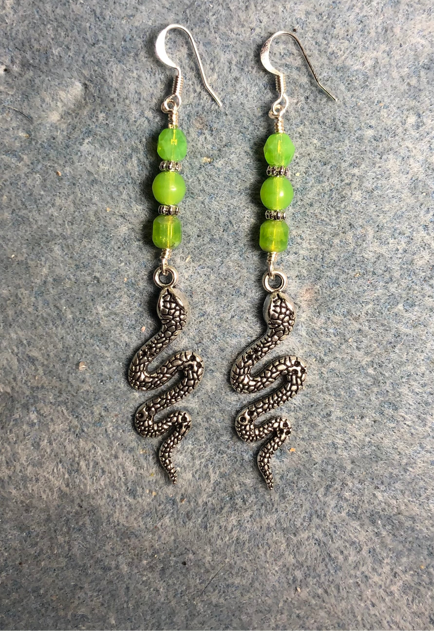 Long silver snake charm earrings adorned with lime green Czech glass beads.