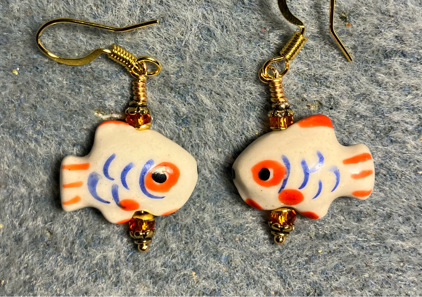 Small white, blue, and orange ceramic fish bead earrings adorned with orange Chinese crystal beads.
