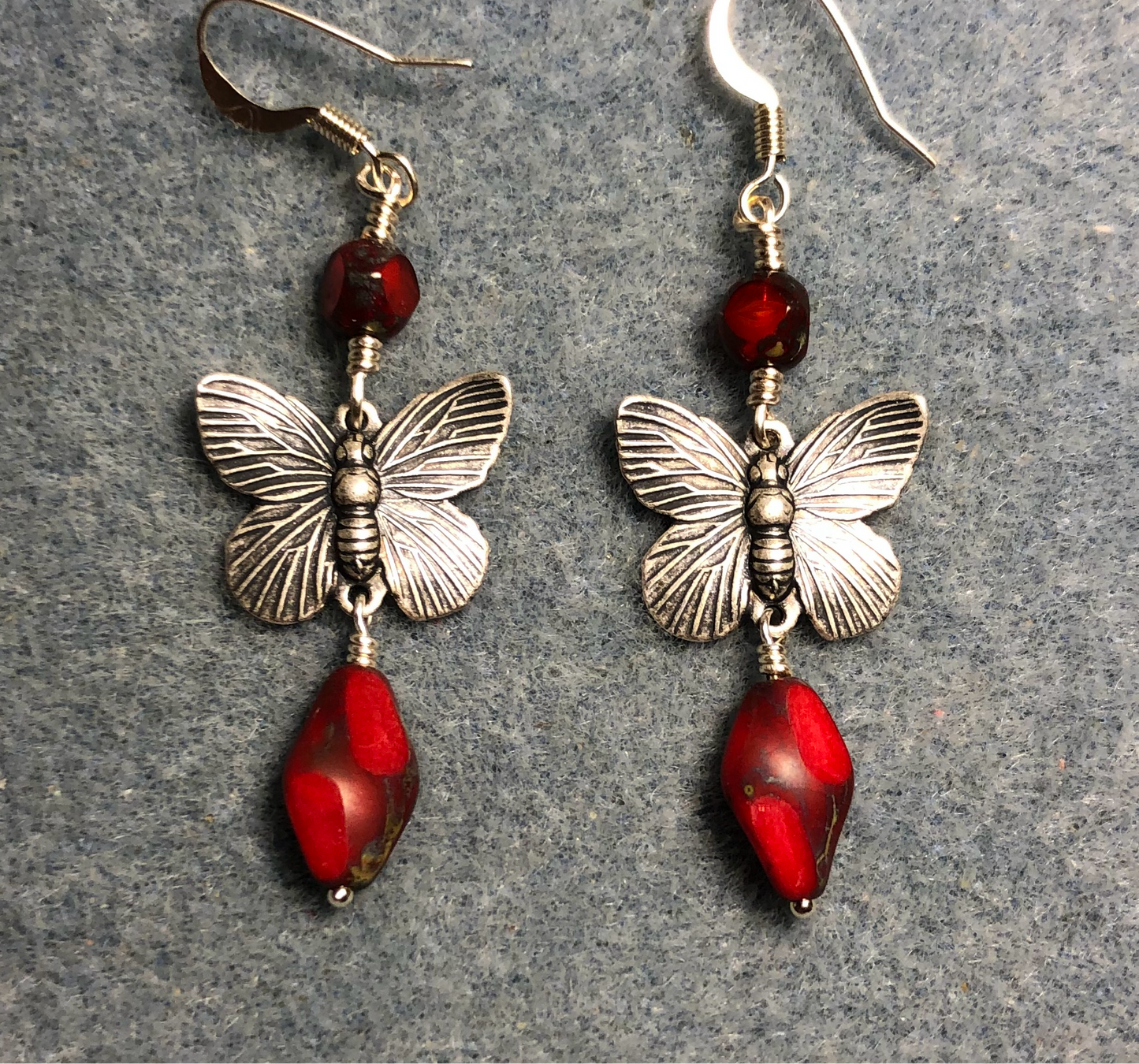 Silver butterfly connector charm earrings adorned with opaque red Czech glass twist beads and opaque red Czech glass beads.