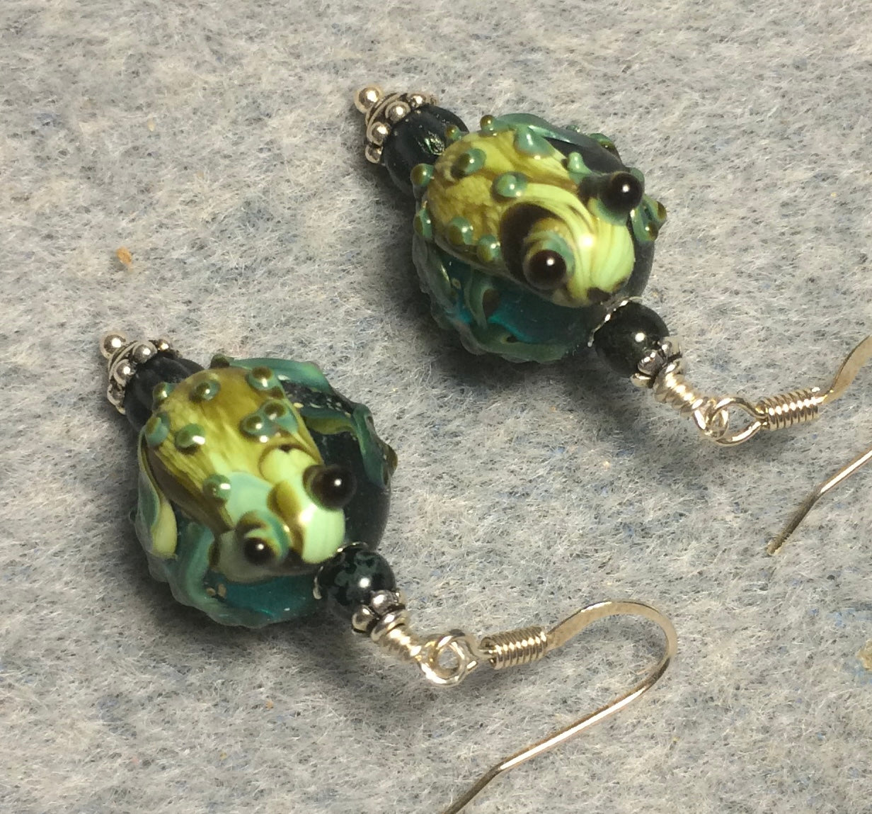 Translucent dark green lamp work frog bead earrings adorned with dark green Czech glass beads.
