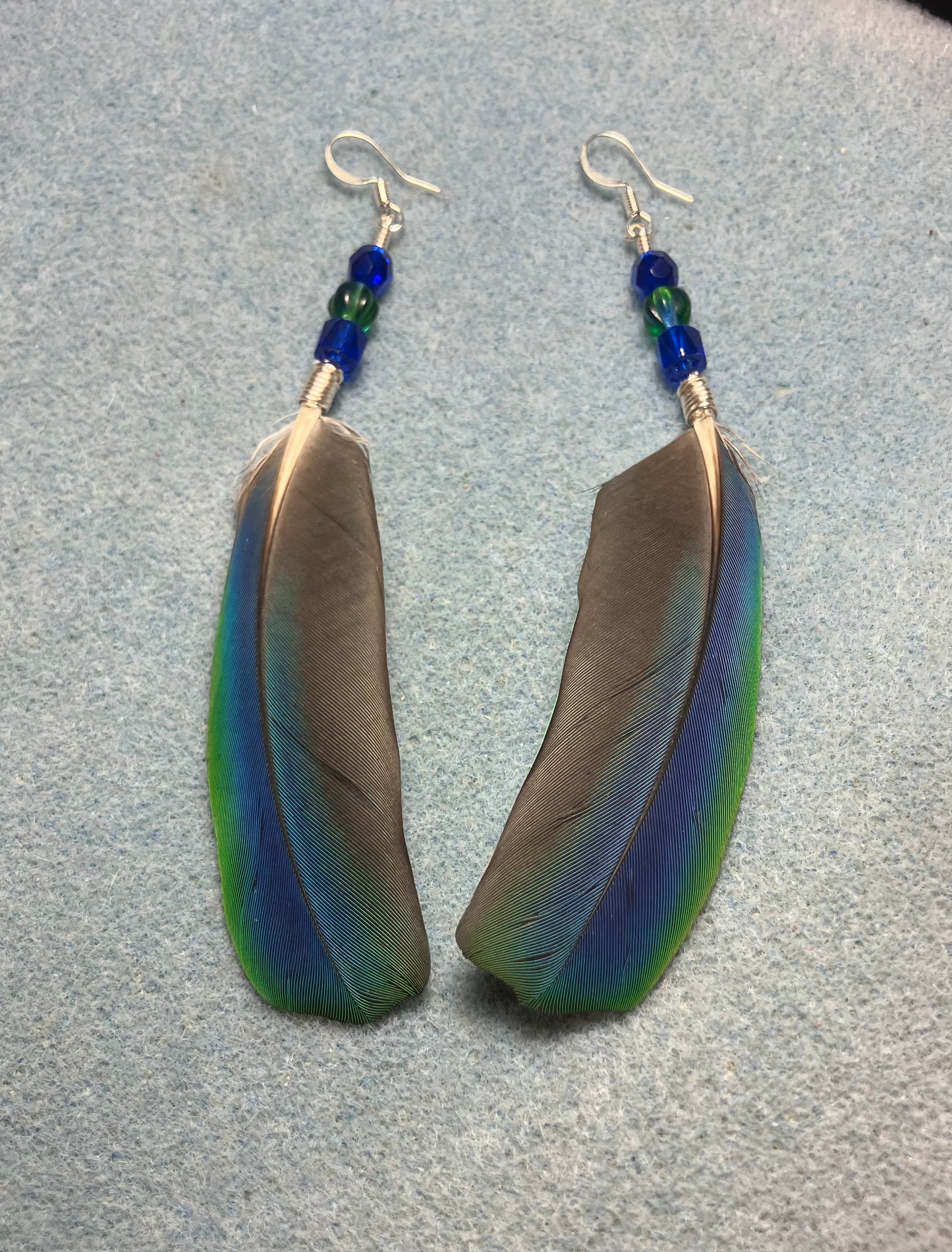Very rare iridescent blue and green Pionus feather earrings adorned with blue and green Czech glass beads.