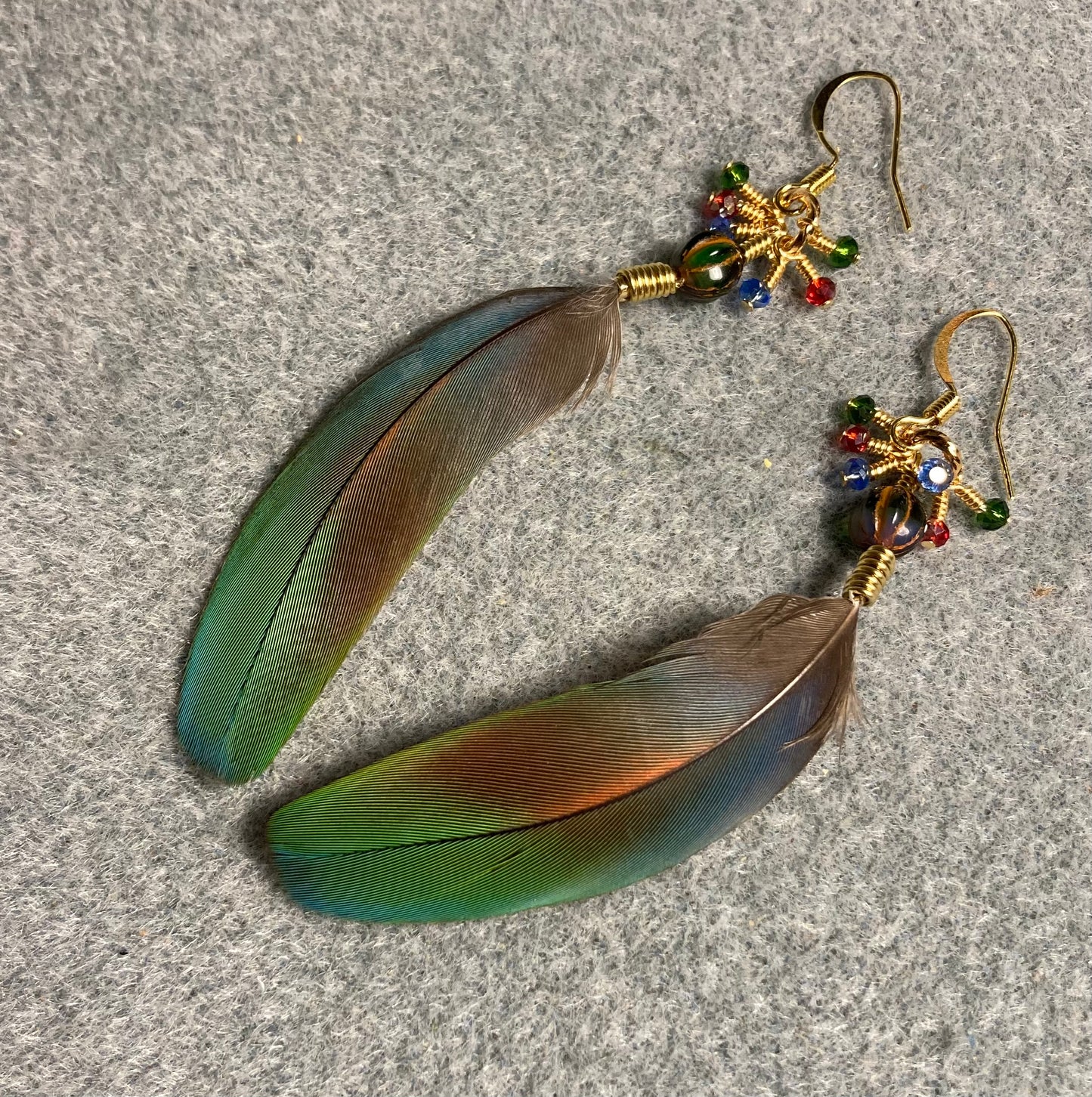 Colorful scarlet macaw feather earrings adorned with green Czech glass beads and tiny dangling green, blue, and red Chinese crystal beads.