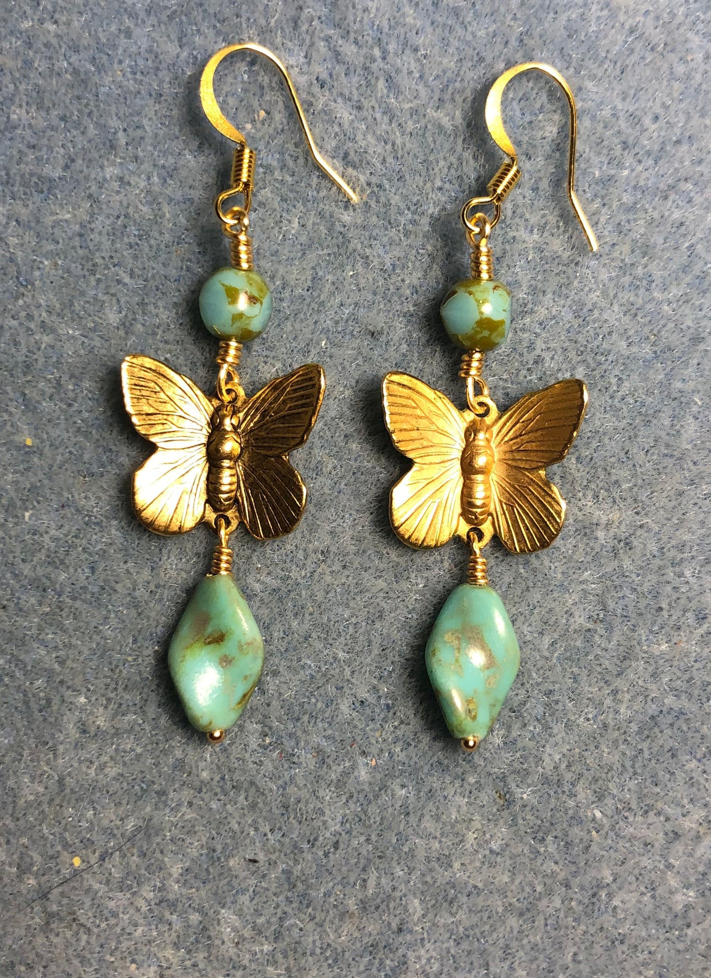 Gold butterfly charm connector earrings adorned with blue green Czech glass twist beads and blue green Czech glass beads.