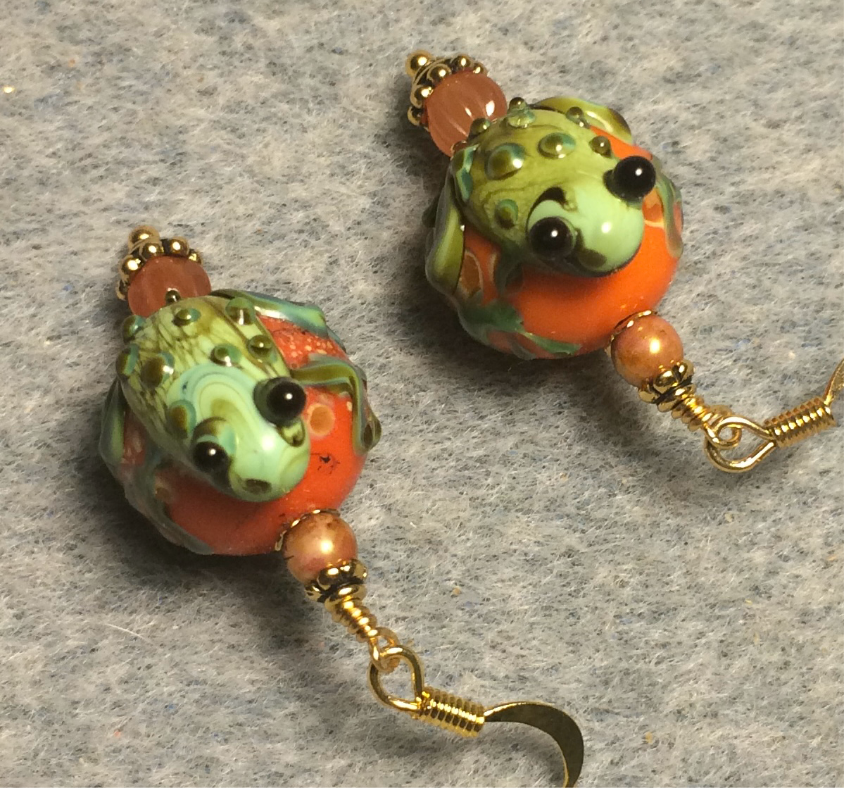 Opaque orange and green lamp work frog bead earrings adorned with orange Czech glass beads.