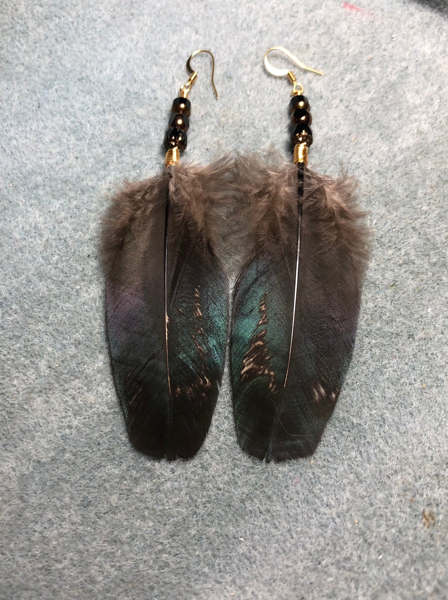 Iridescent black, gold, and green rooster feather earrings adorned with black and gold Czech glass beads.