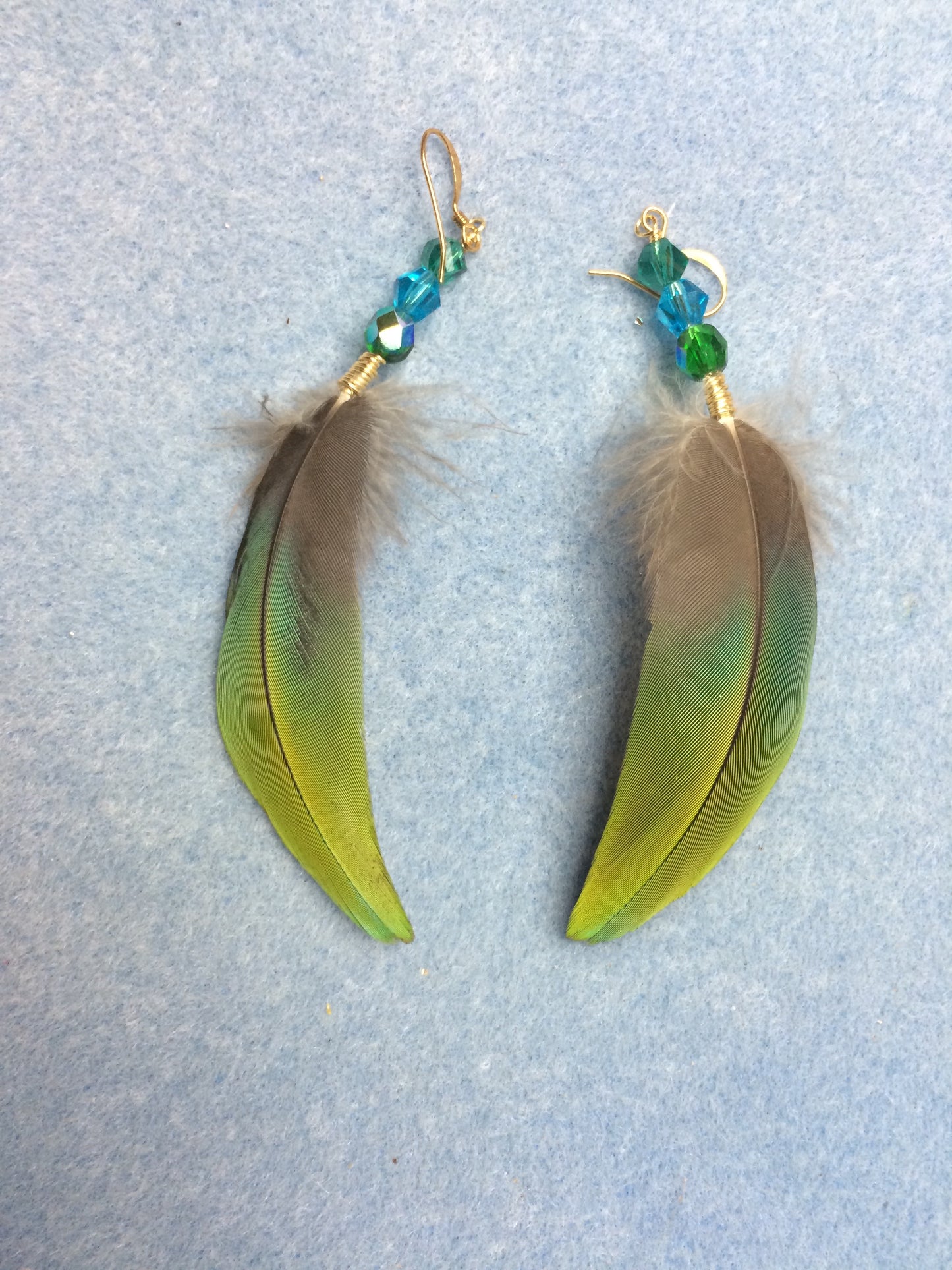 Green and blue macaw feather earrings adorned with blue, green, and teal Czech glass beads.