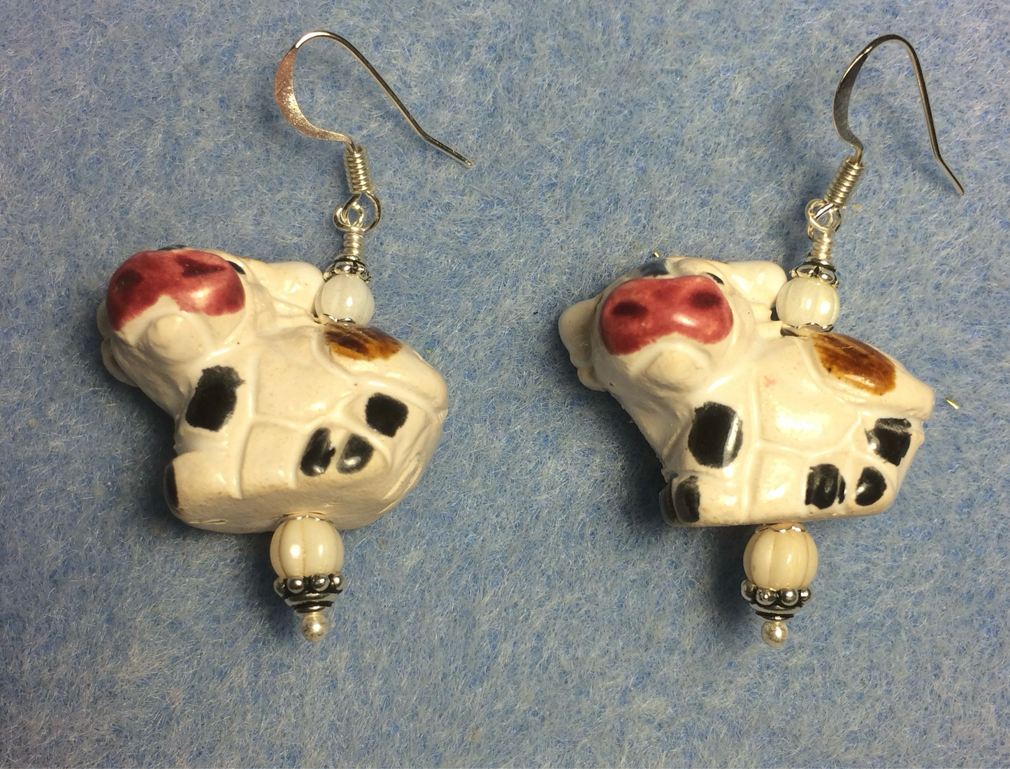 White, black, brown, and pin ceramic cow bead earrings adorned with white Czech beads.