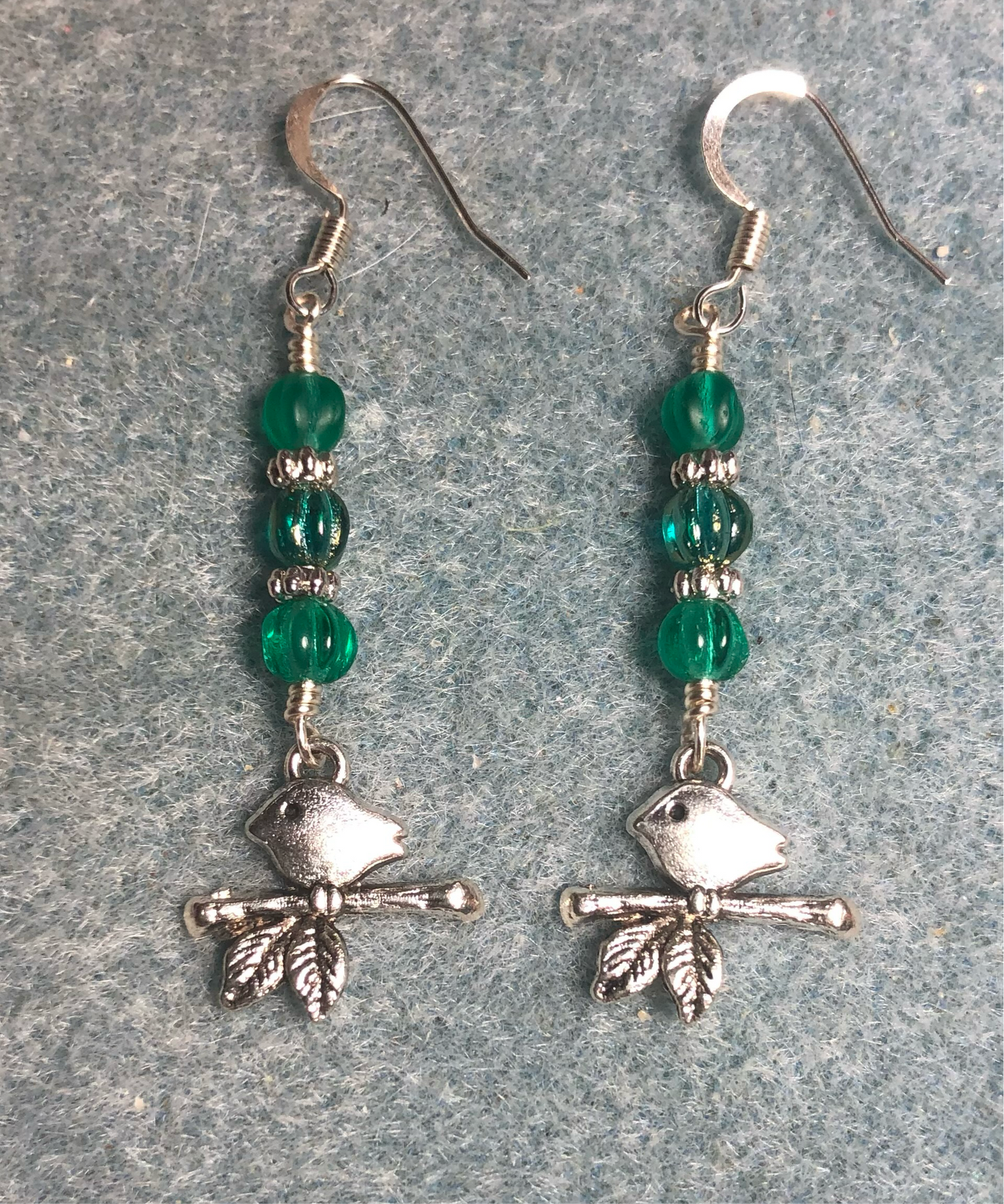 Small silver bird sitting on a branch charm earrings adorned with small teal Czech glass melon beads