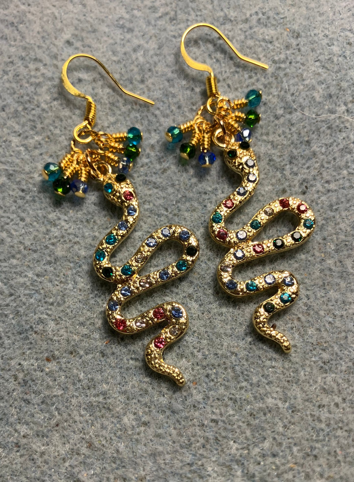 Gold and colored rhinestone coiled snake charm earrings adorned with tiny dangling turquoise, light blue, and dark green Chinese crystal beads.