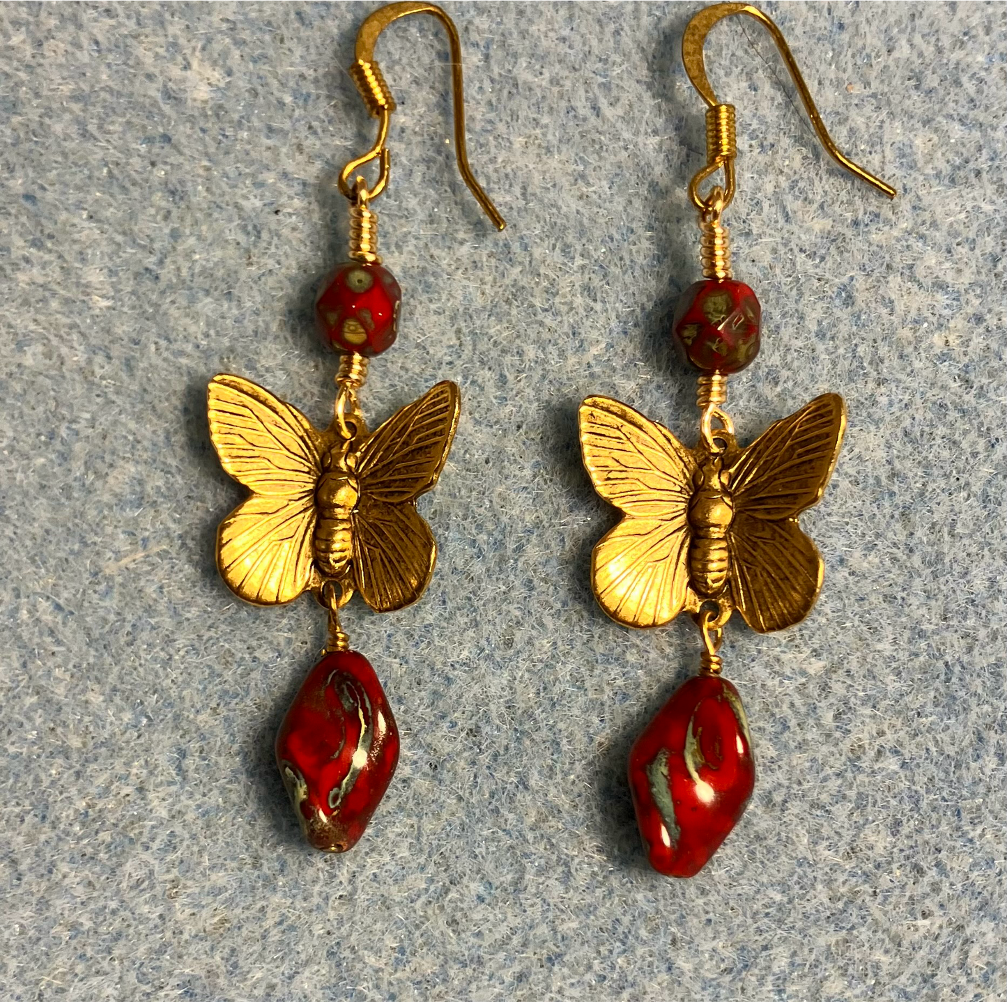 Gold butterfly charm connector earrings adorned with red Picasso Czech glass twist beads and red Picasso Czech glass beads.