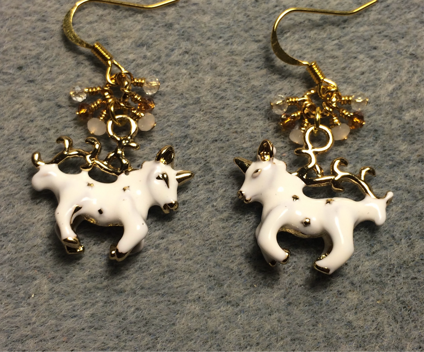 White and gold enamel unicorn charm earrings adorned with tiny dangling white, amber, and clear Chinese crystal beads.