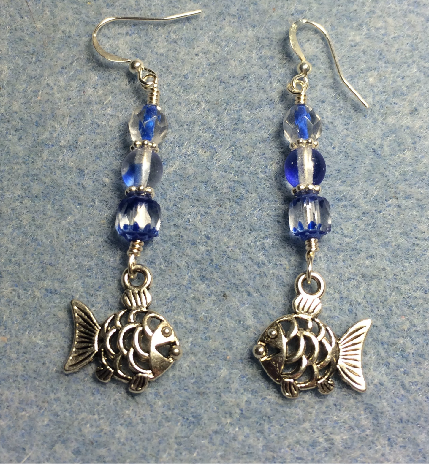 Silver fish charm earrings adorned with blue Czech glass beads.
