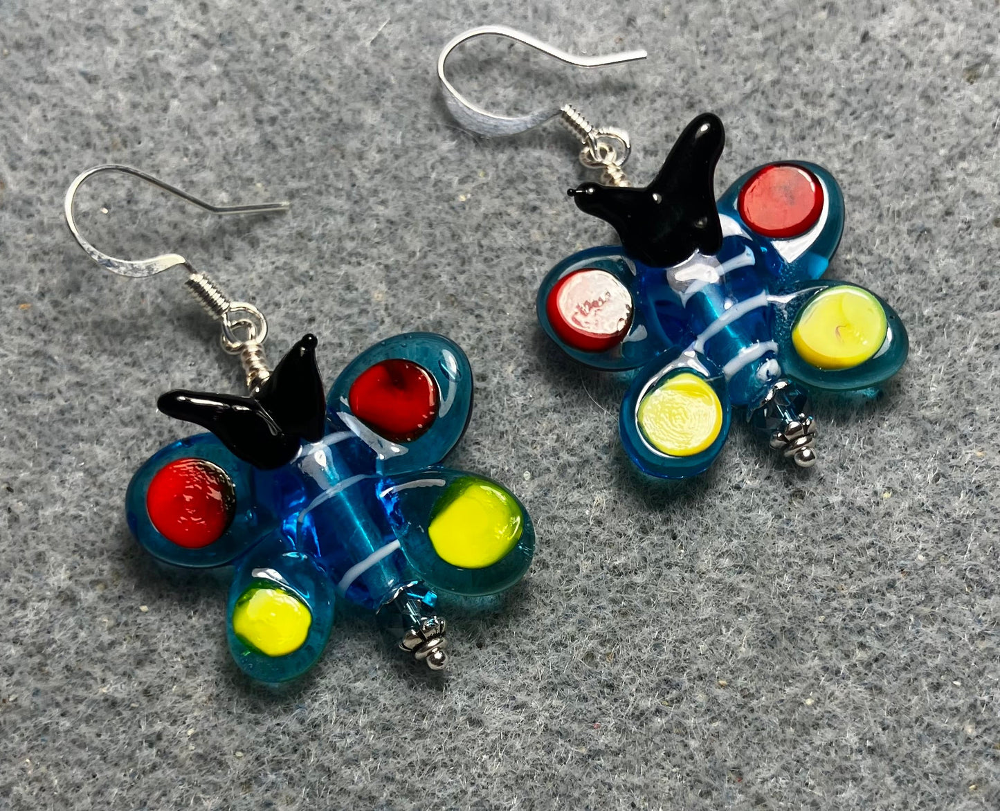 Turquoise, red, yellow, and black lamp work butterfly bead earrings adorned with turquoise Czech glass beads.