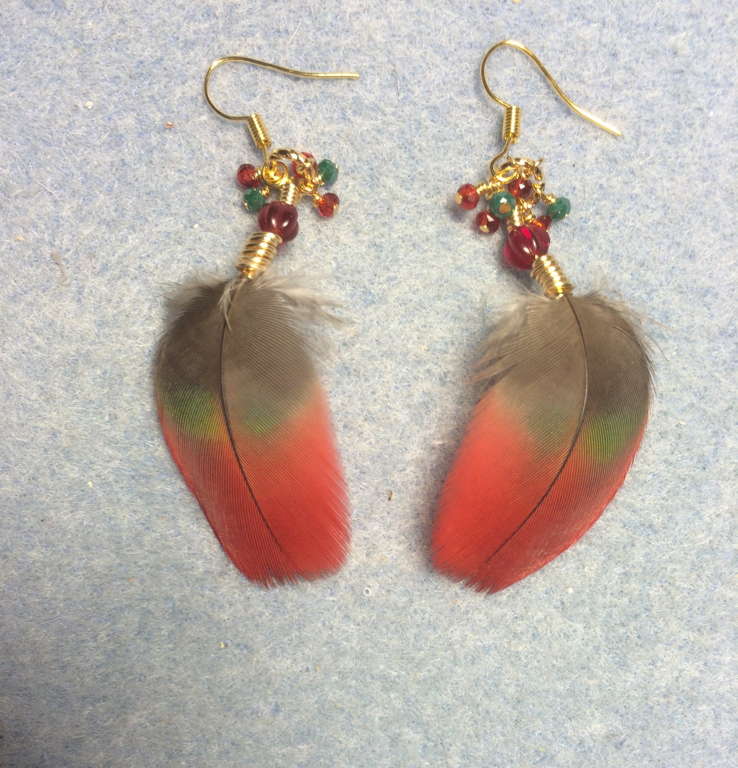 Small red and dark green macaw feather earrings adorned with red Czech glass beads and tiny dangling red and green Chinese crystal beads.