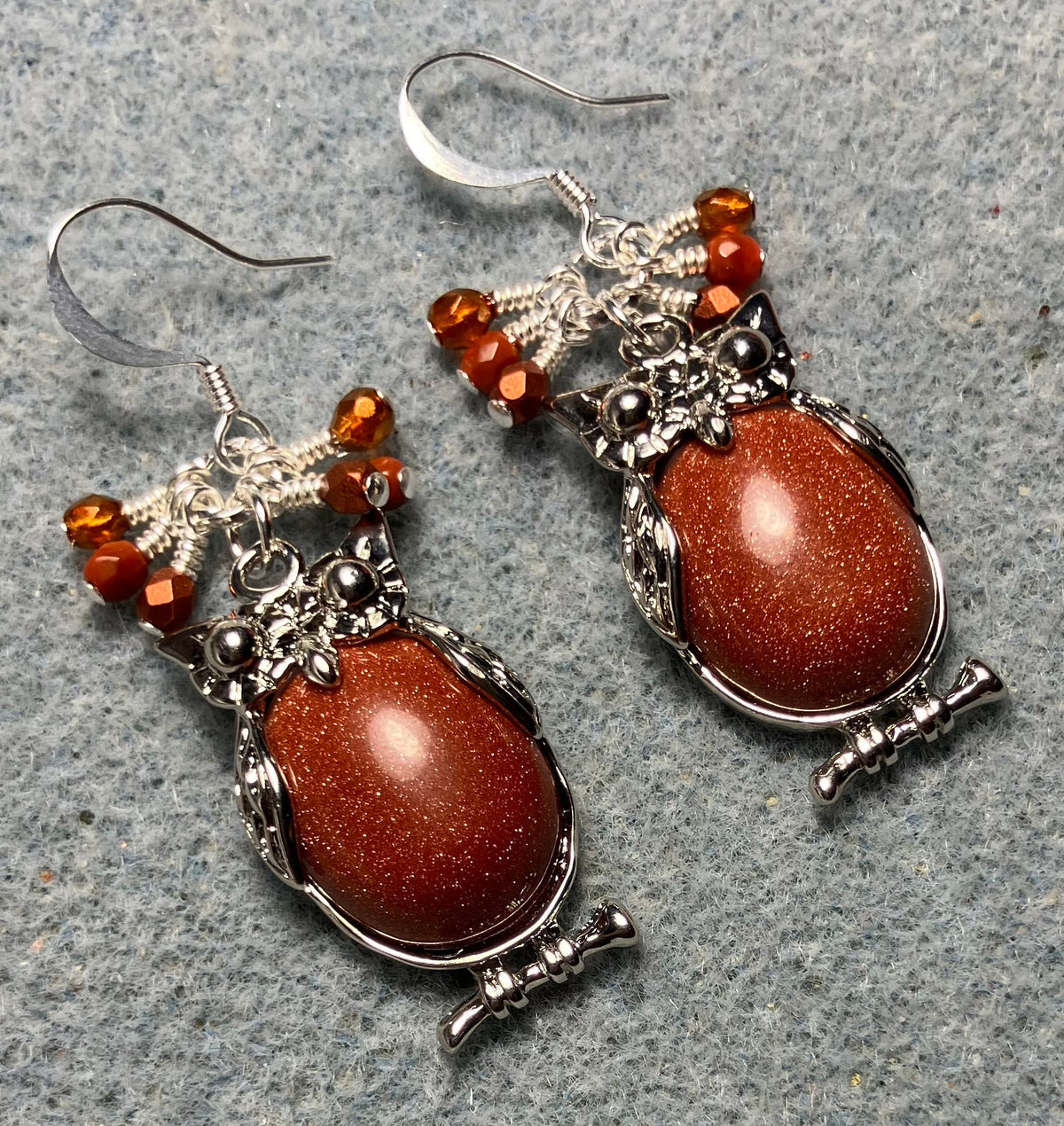 Large silver and orange goldstone gemstone owl charm earrings adorned with small dangling orange Czech glass beads.