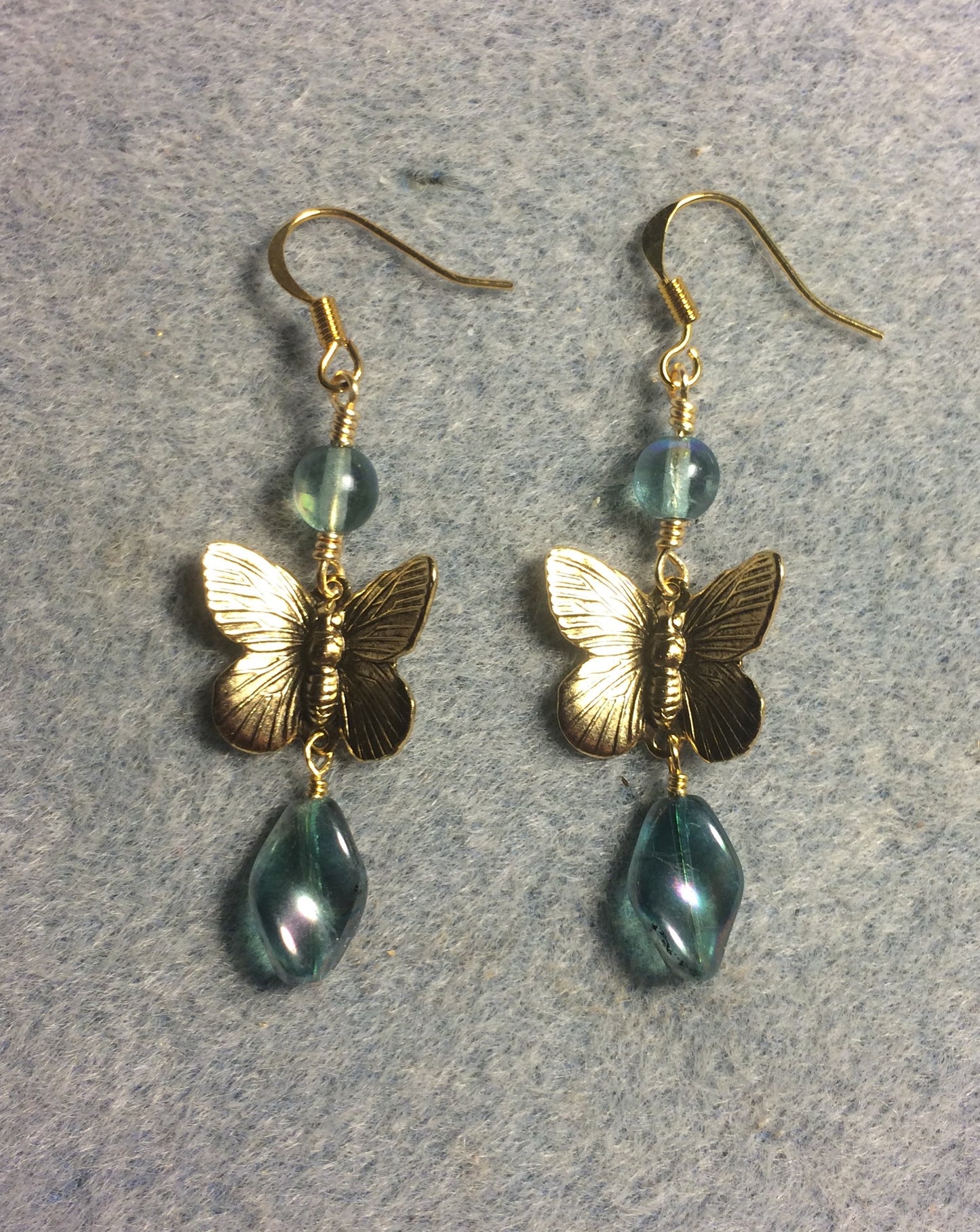 Gold butterfly charm connector earrings adorned with smoky blue green Czech glass twist beads and smoky blue green Czech glass beads.