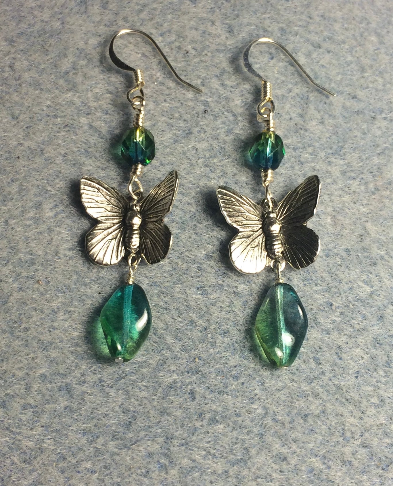 Silver butterfly charm connector earrings adorned with blue green Czech glass twist beads and blue green Czech glass beads.