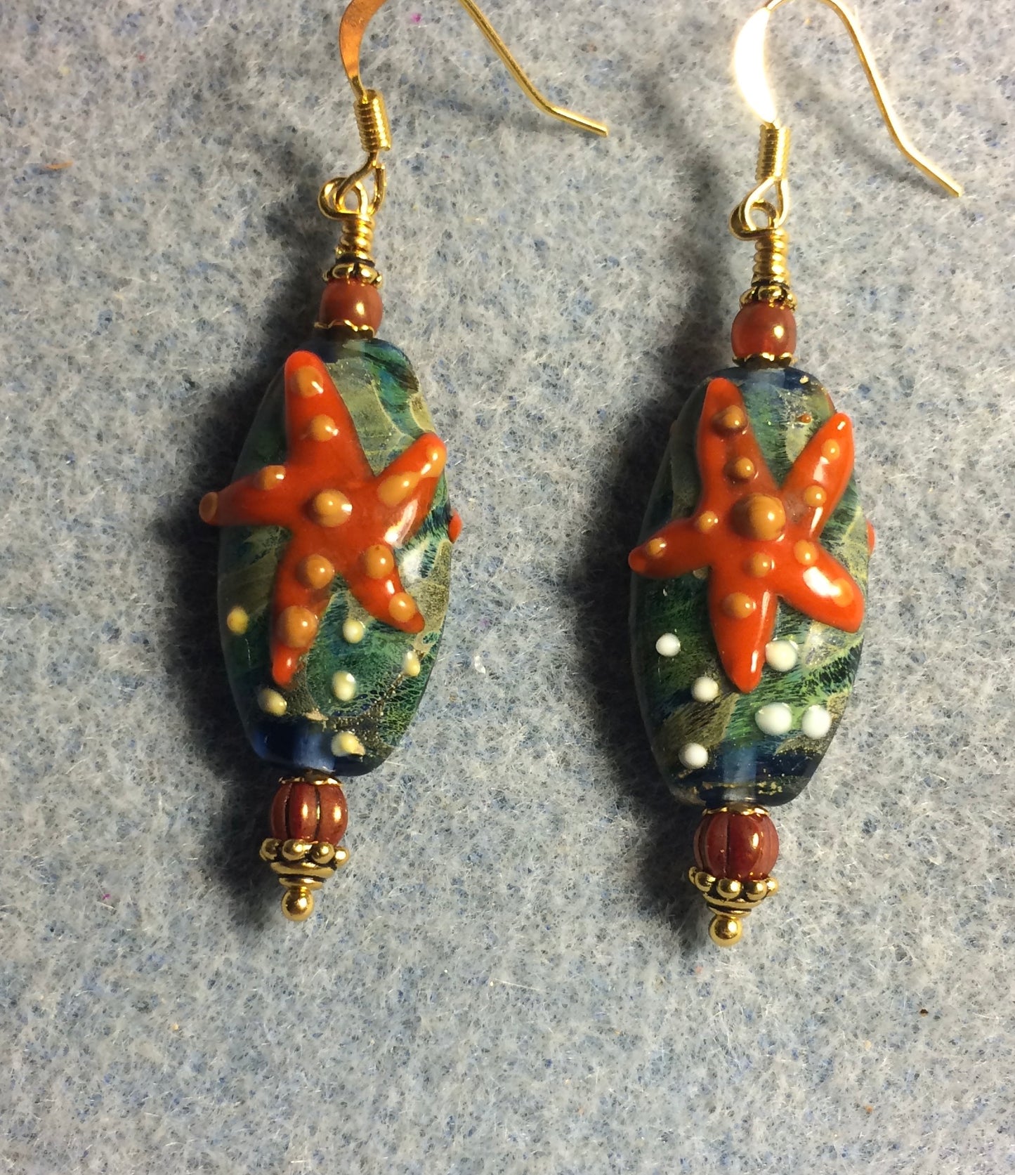 Blue green and orange lamp work starfish bead earrings adorned with dark orange Czech glass beads.