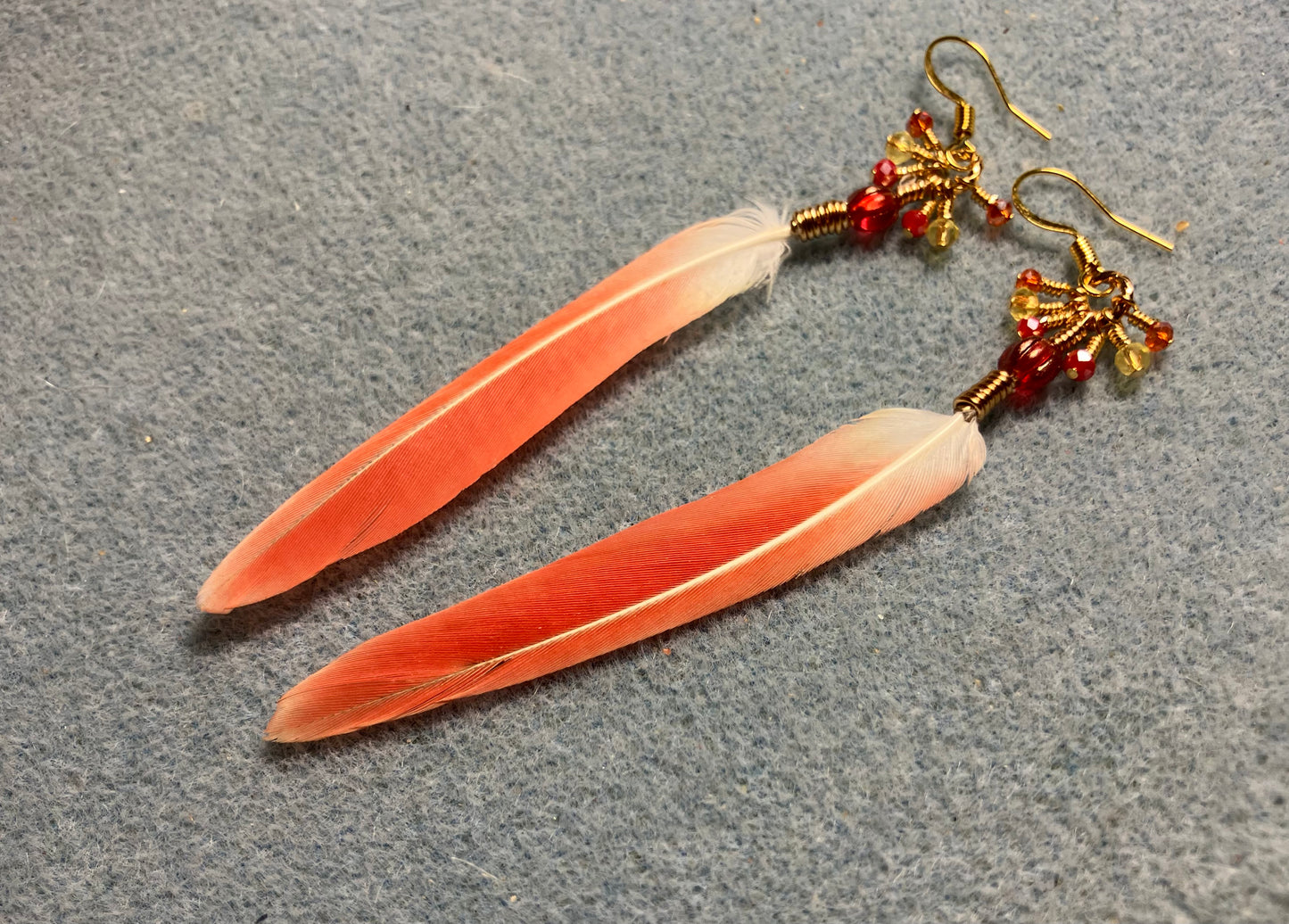Small bright red sun cheeked conure feather earrings adorned with red Czech glass melon beads and tiny dangling red and yellow Chinese crystal beads.