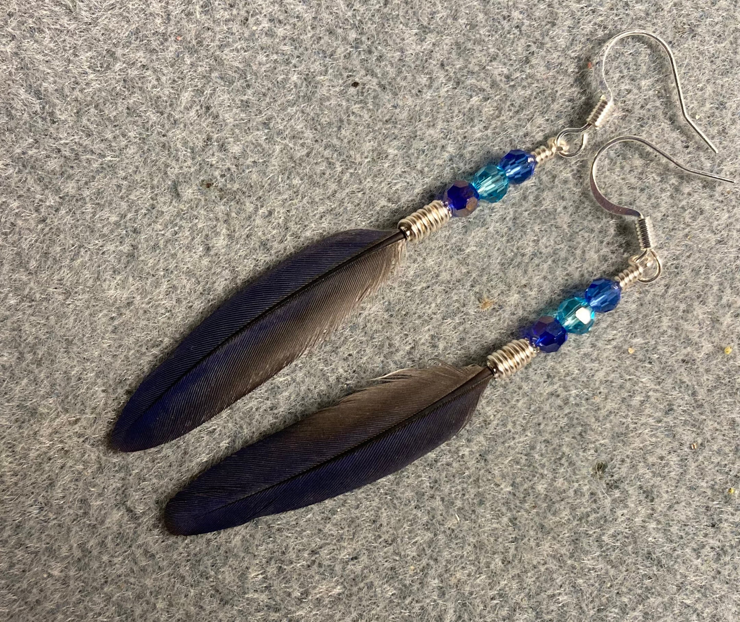 Small rare iridescent blue Pionus parrot feather earrings adorned with small dark blue and turquoise Chinese crystal beads.