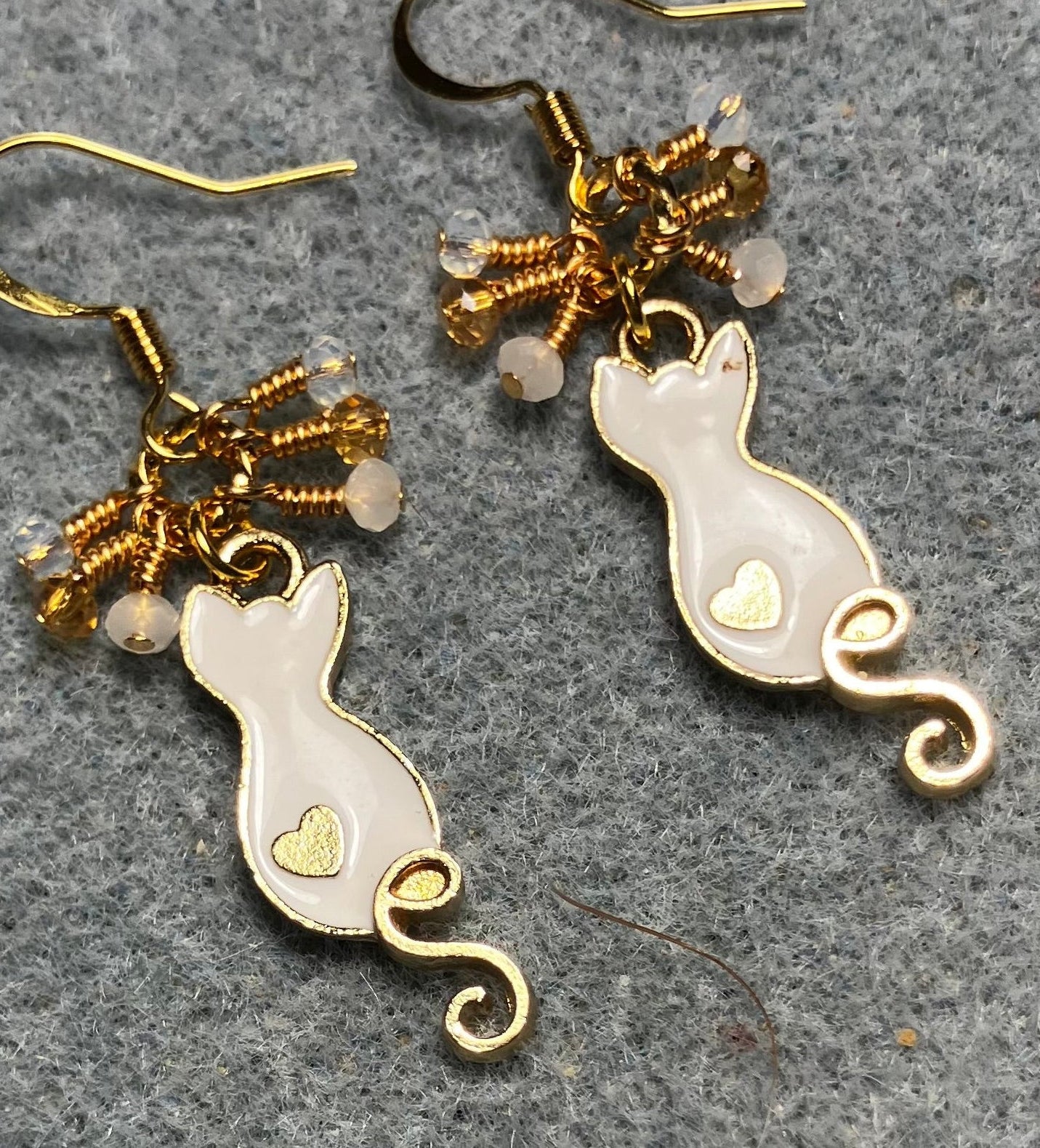 Small white and gold enamel curly tailed cat charm earrings adorned with tiny dangling white, amber, and clear Chinese crystal beads.