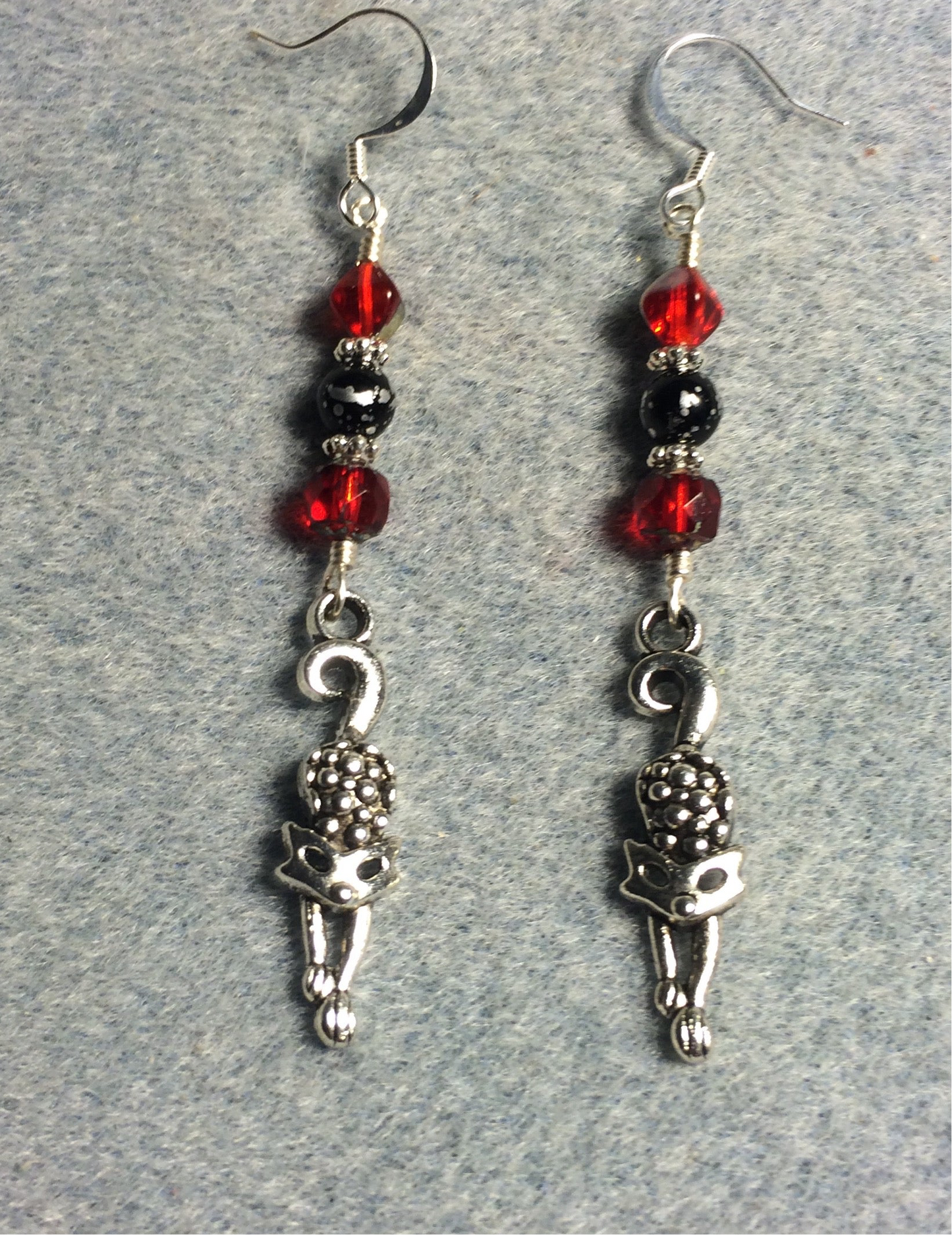 Silver stretching cat charm earrings adorned with red and black Czech glass melon beads.