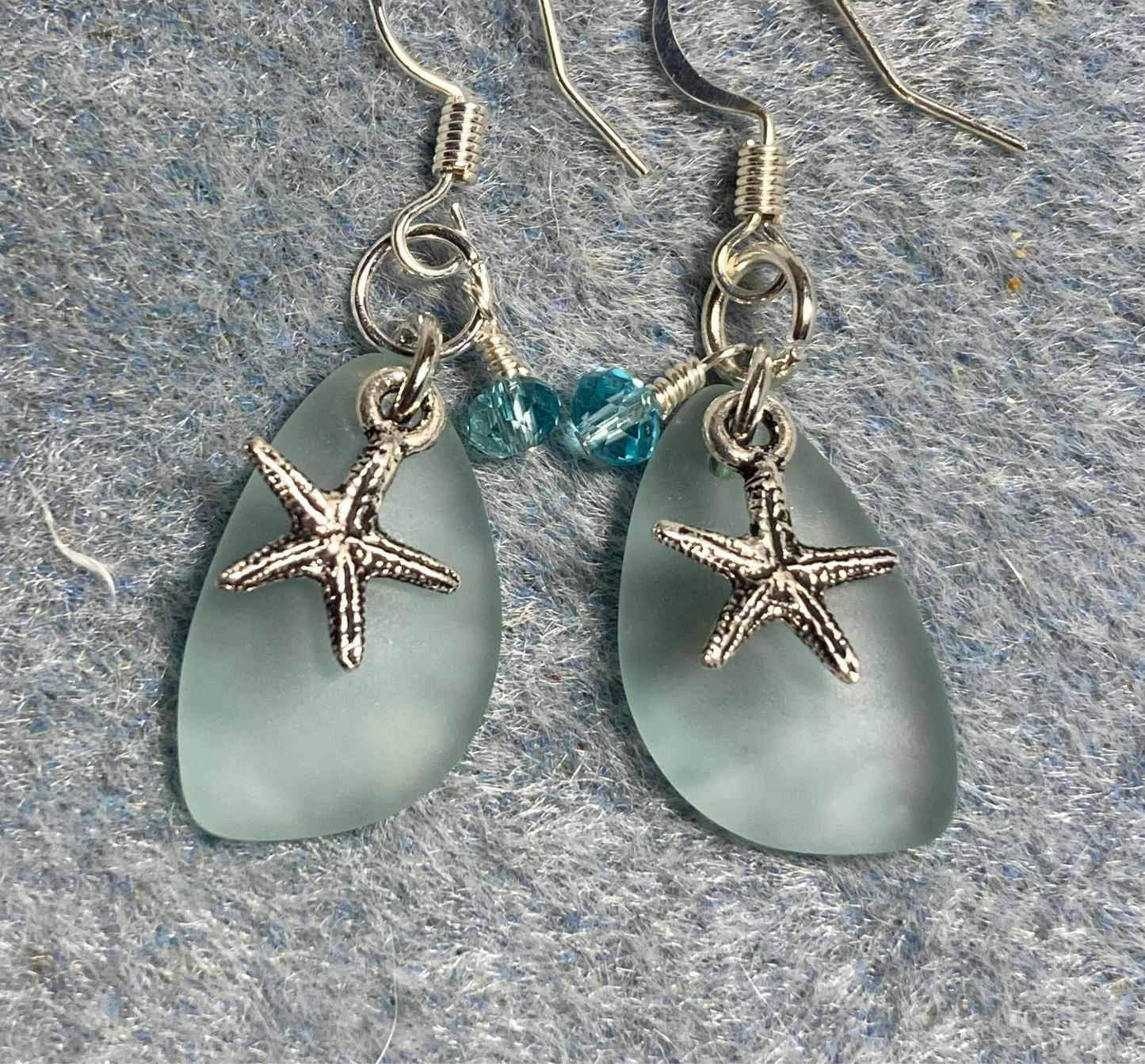 Small light green sea glass pendant bead earrings adorned with small silver starfish charms and light aqua Chinese crystal beads.
