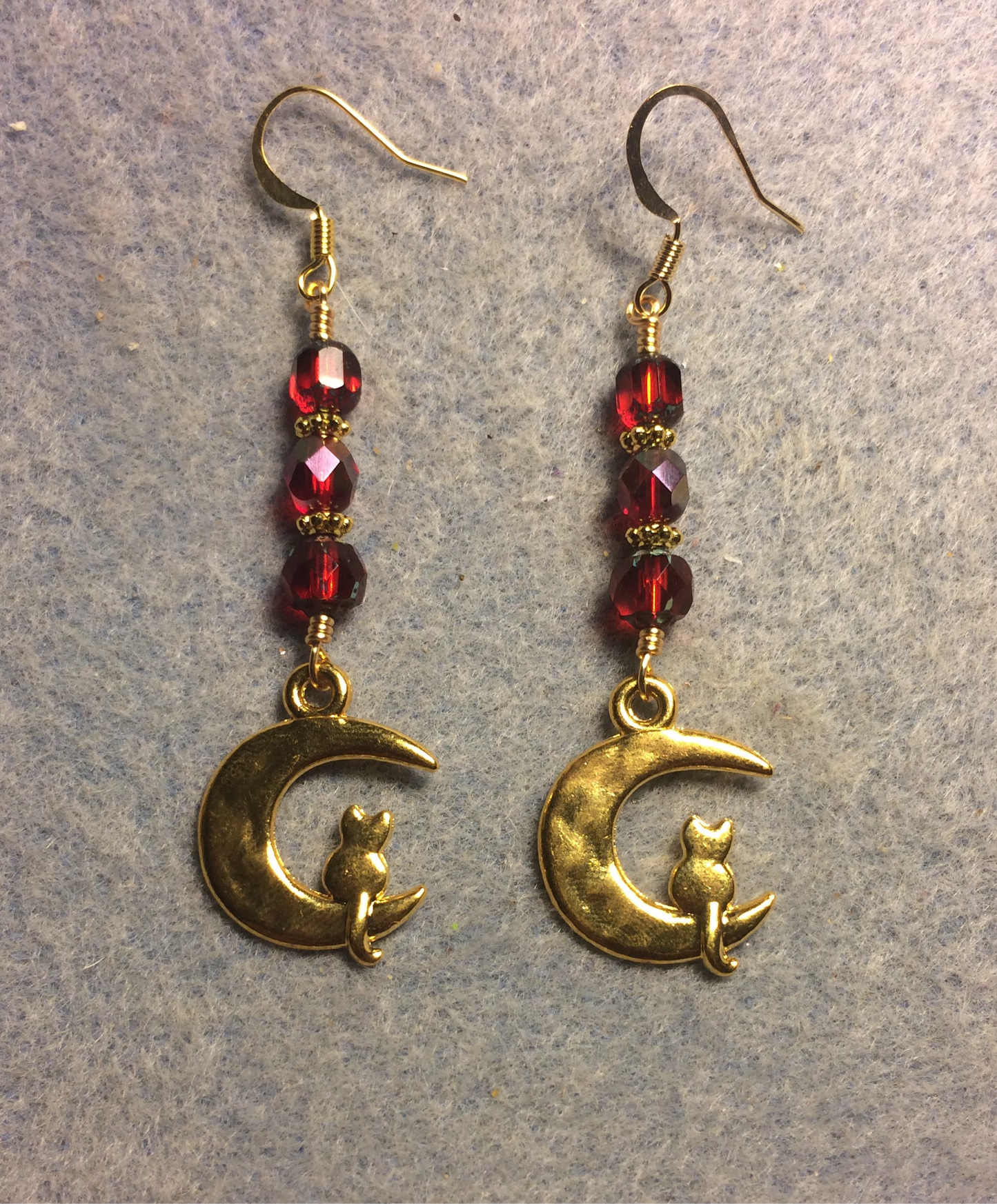 Gold cat sitting on a quarter moon charm earrings adorned with red Czech glass beads