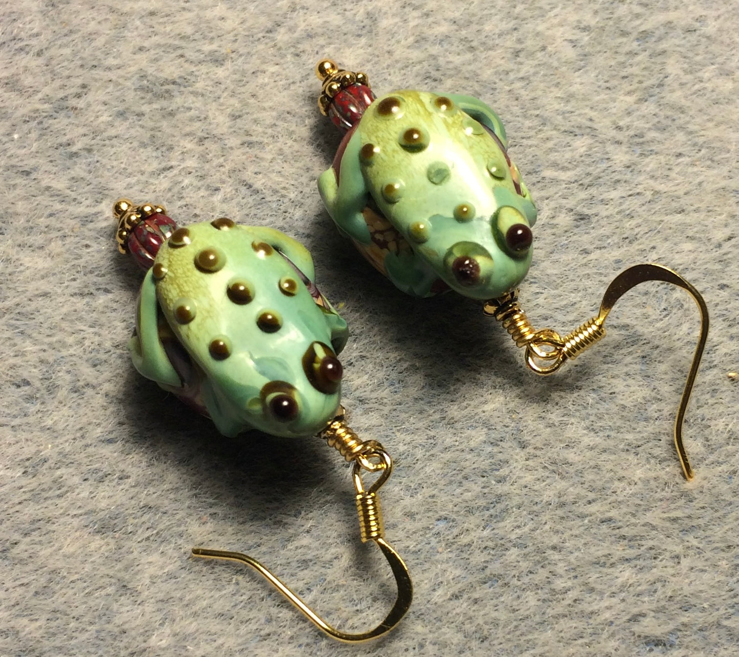 Large green and dark red lamp work frog bead earrings adorned with red Picasso Czech glass beads.