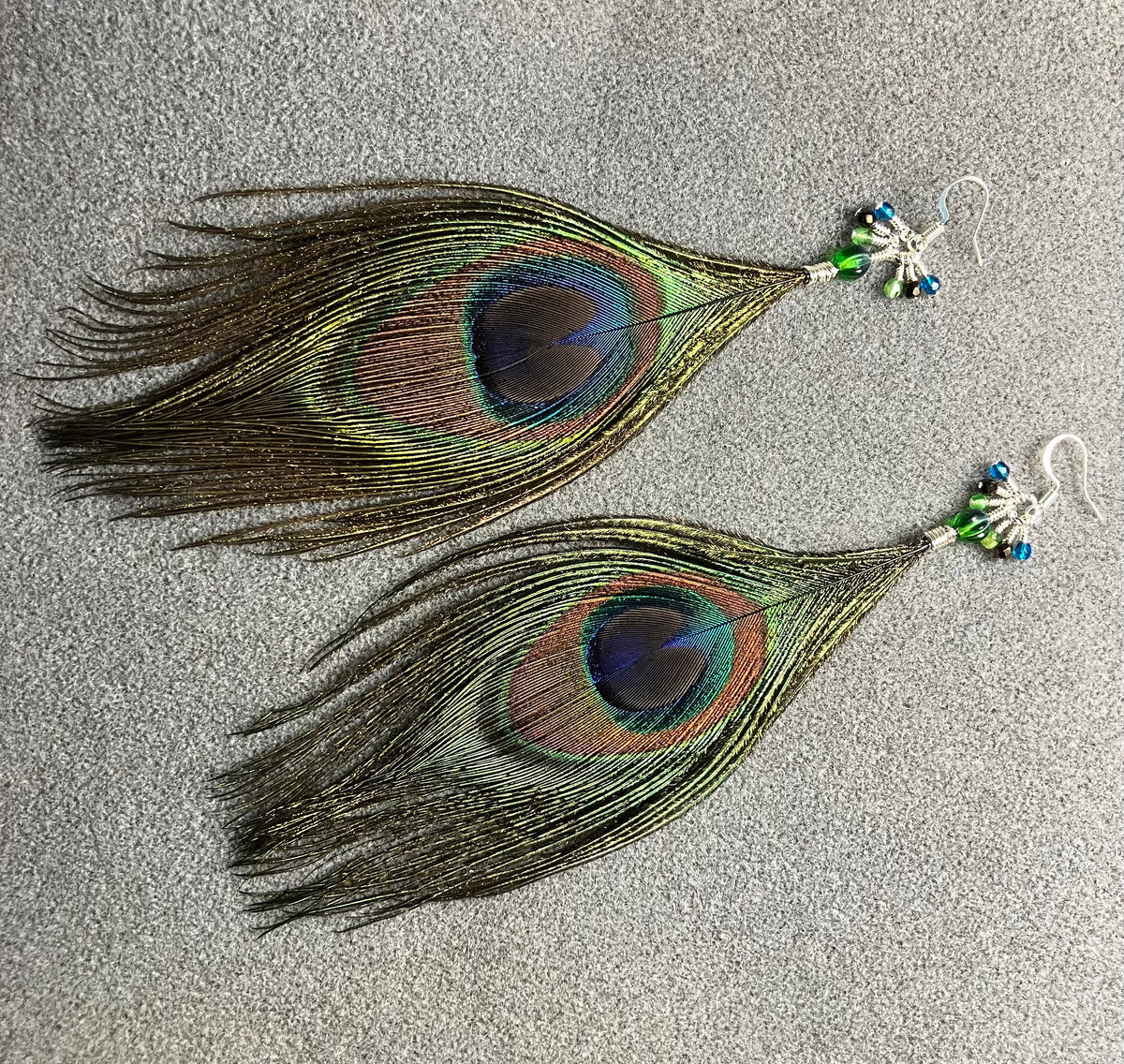 Peacock eye feather earrings adorned with small dangling green, brown, and teal Czech glass beads.
