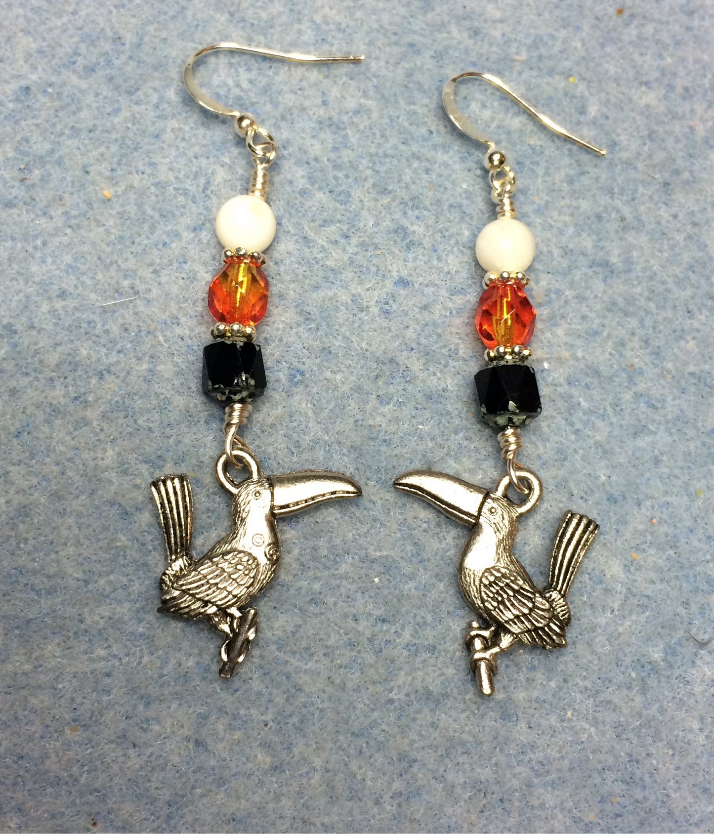 Silver toucan charm earrings adorned with black, orange, and white Czech glass beads