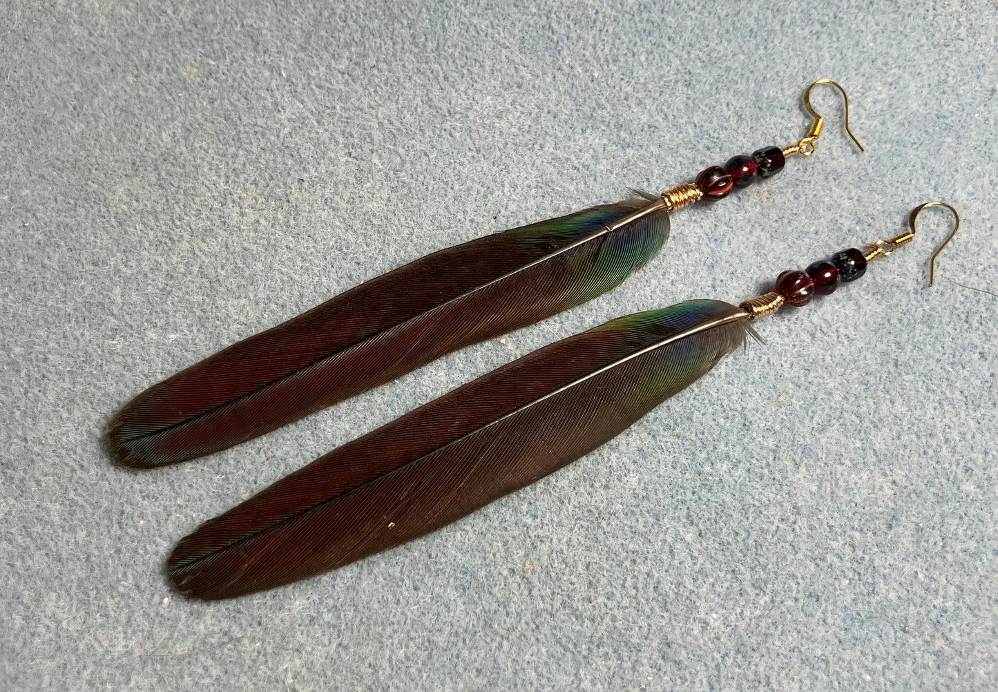 Dark red crimson bellied conure feather earrings adorned with dark red Czech glass beads.